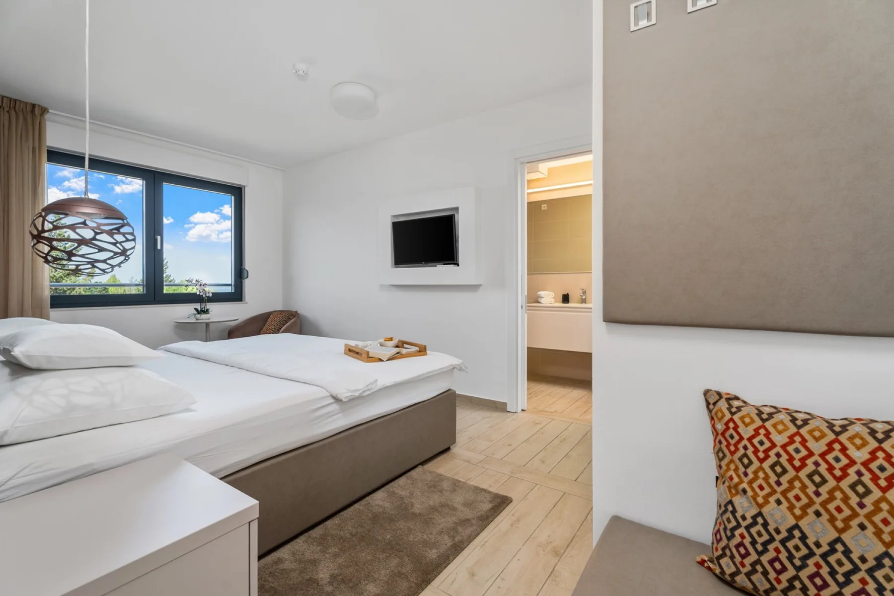 A bright bedroom with a large bed beside a window and an open doorway.
