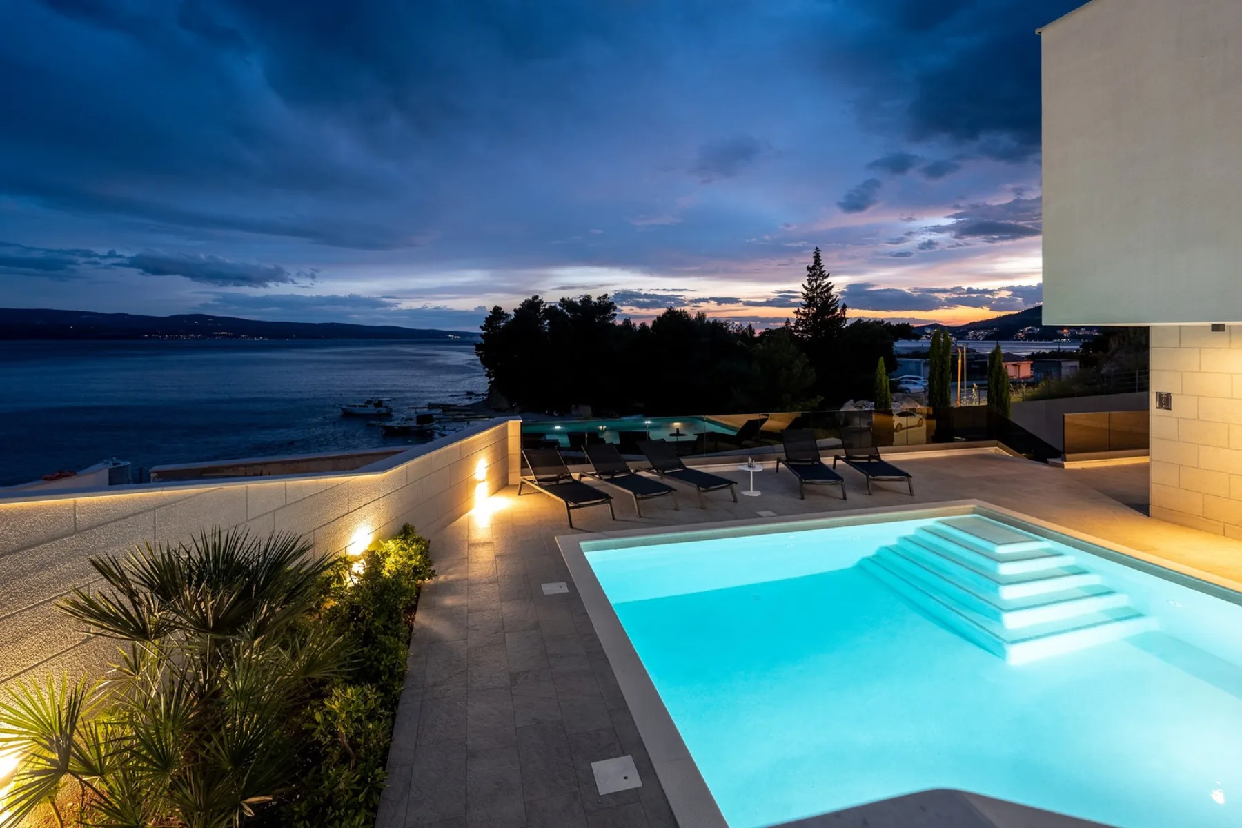 An outdoor pool and deck overlook the water beneath a colorful evening sky.