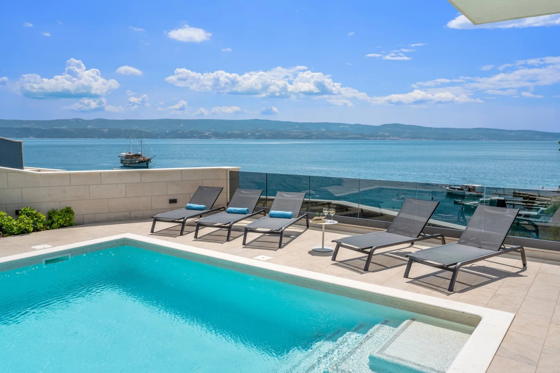 A seaside pool terrace overlooks the water, with lounge seating along the edge.