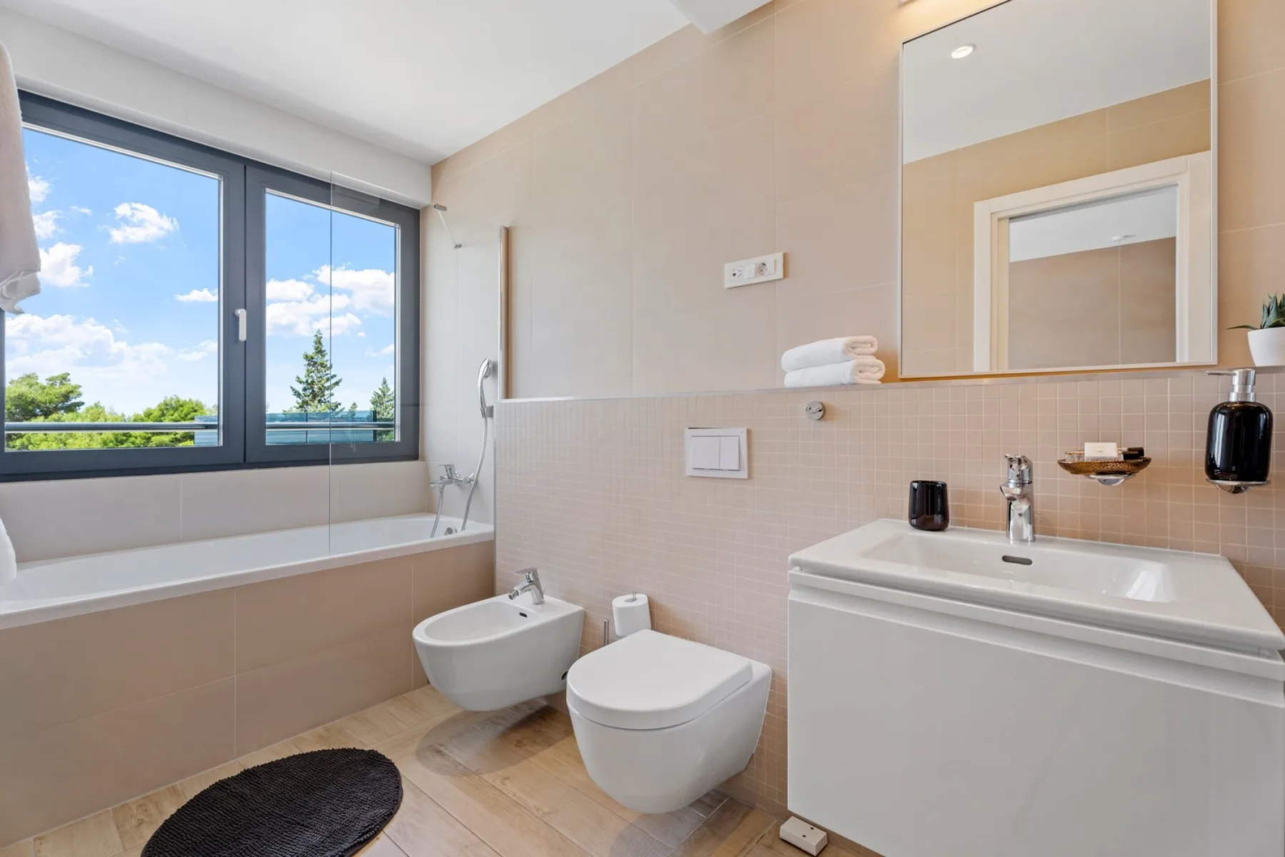 A bright bathroom with a bathtub, toilet, bidet, and sink beneath a large mirror.