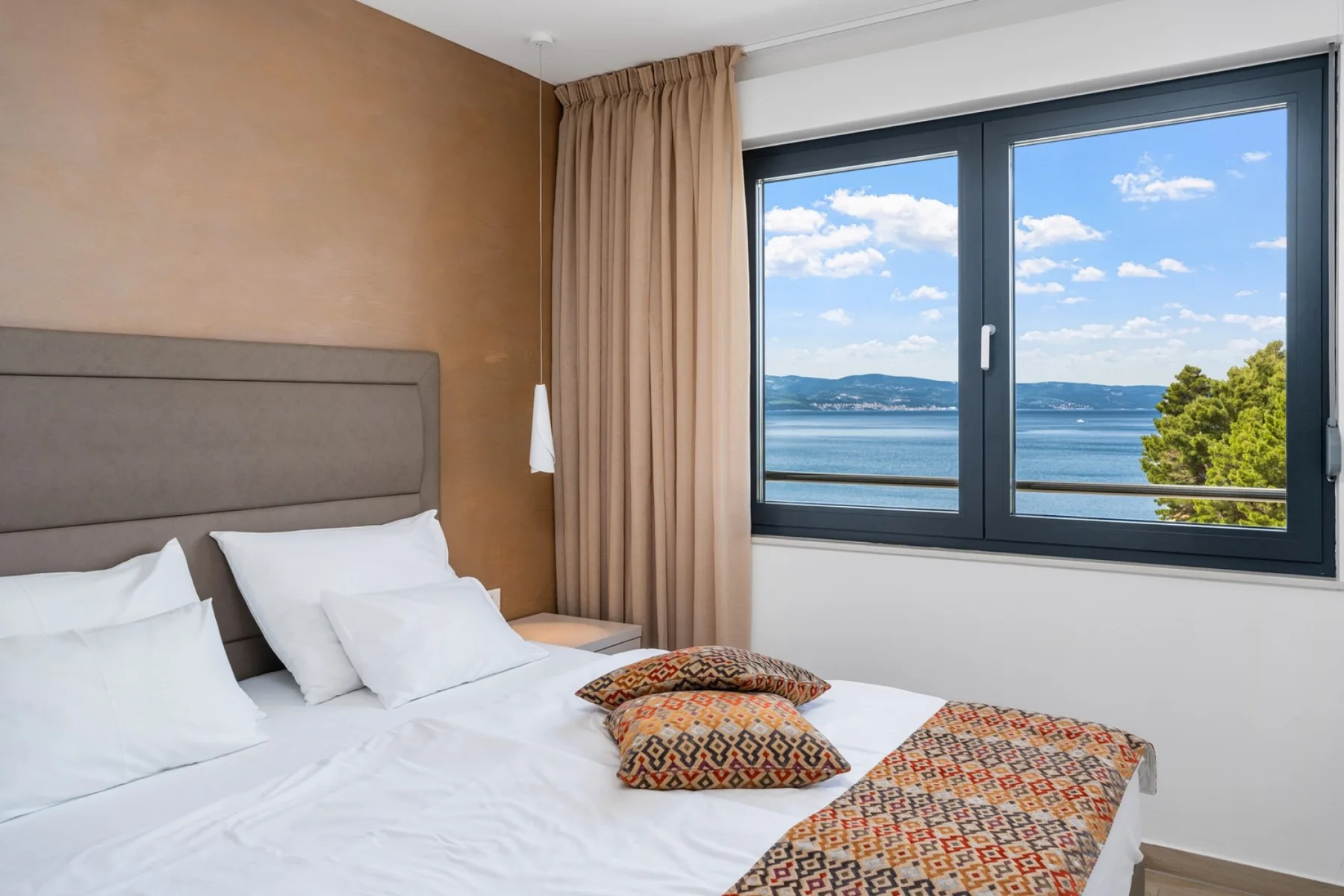 A bedroom with a bed beside a large window overlooking the water.