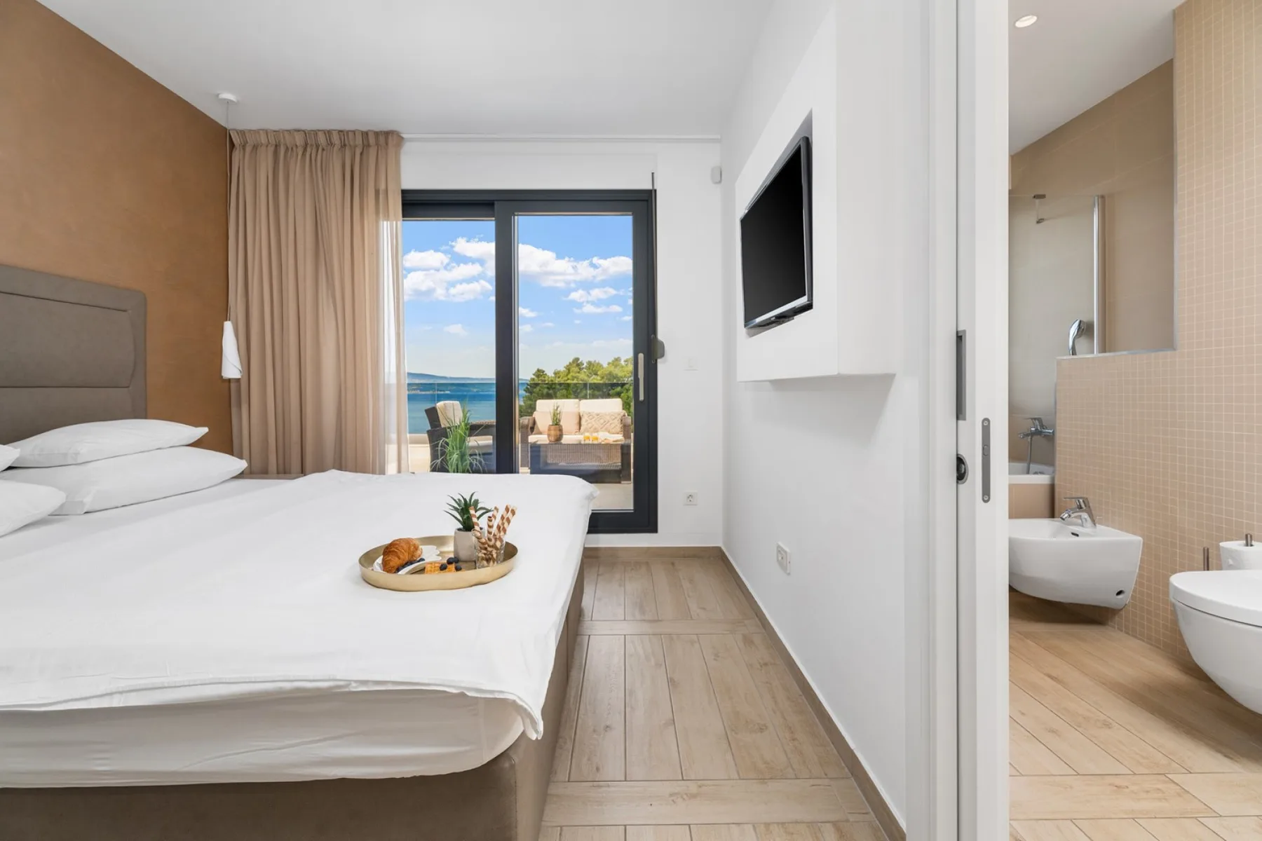 A bright bedroom with a bed beside a large window overlooking the water.