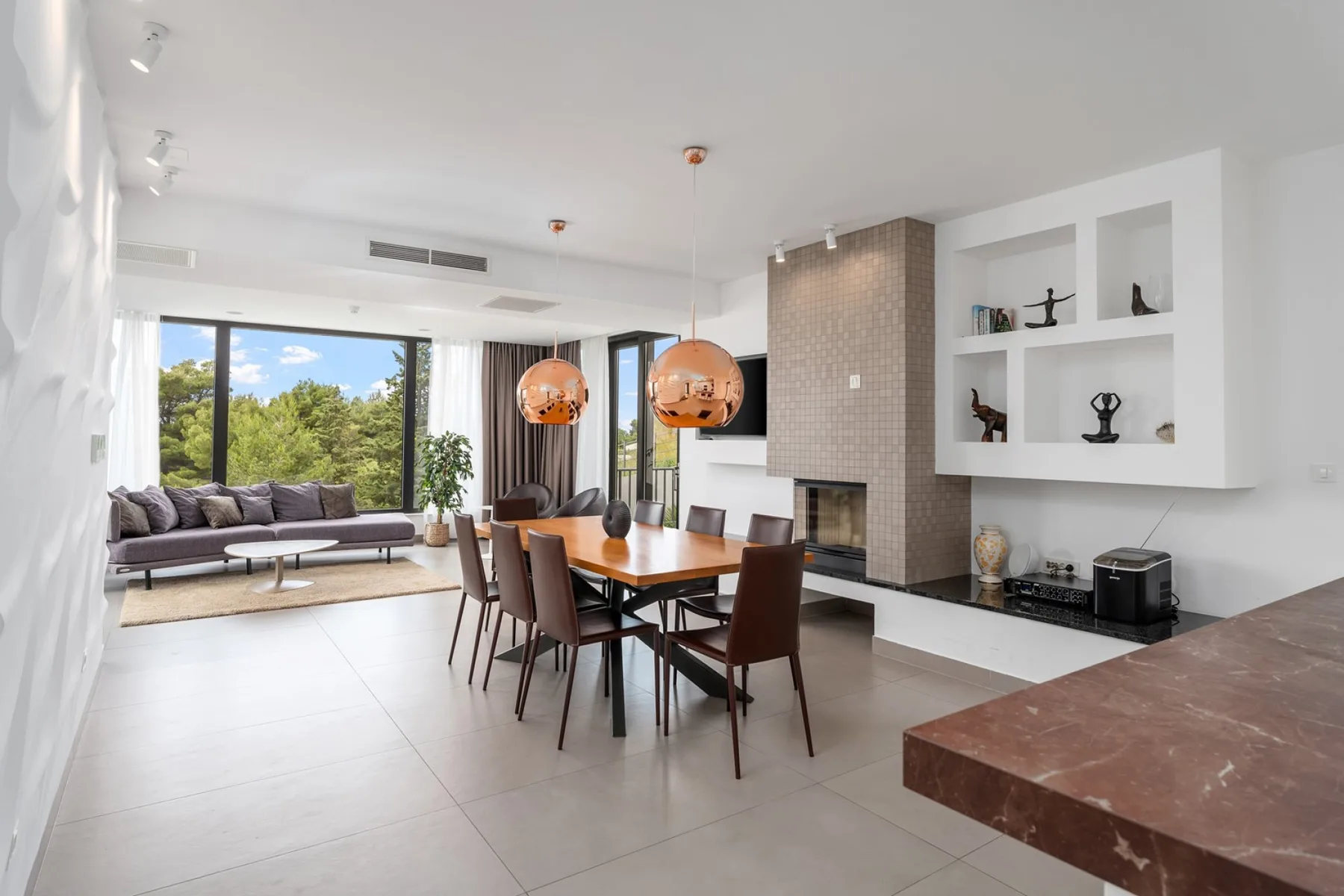 A bright open-plan living and dining room with large windows and a fireplace.
