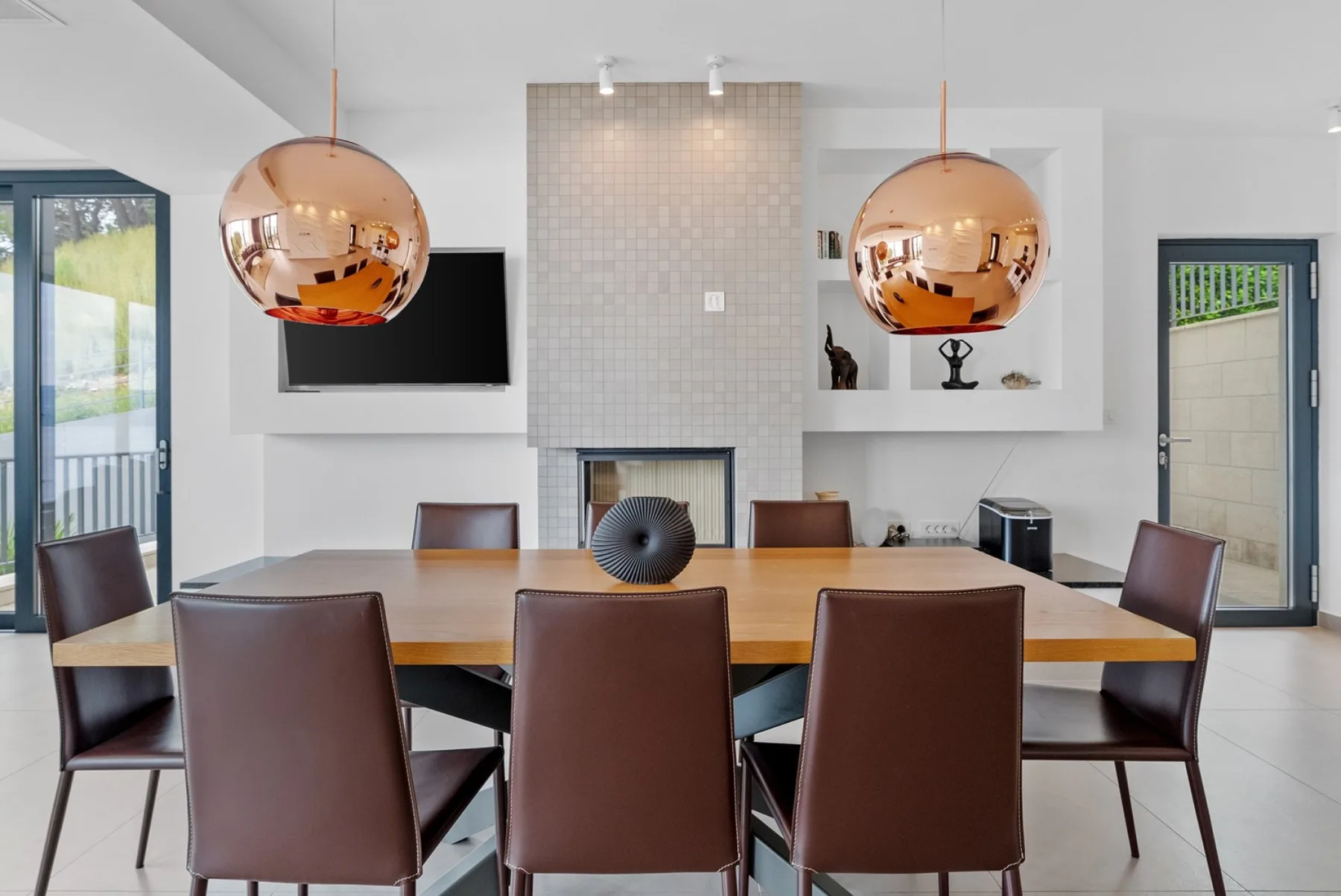 A dining area with a long table, brown seating, and two pendant lights.