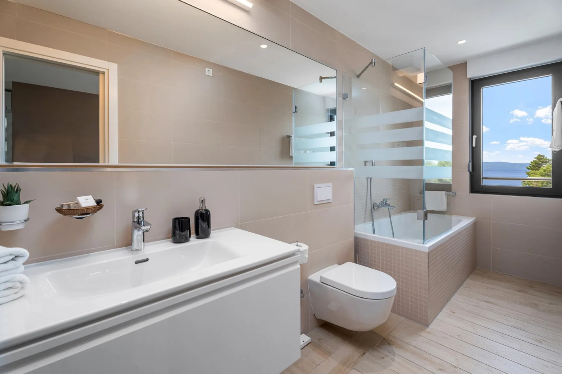 A bright bathroom features a bathtub with a glass shower screen and a wide sink.