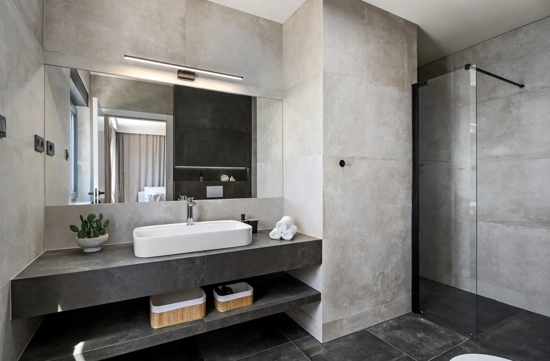 A modern bathroom with a wide stone vanity, vessel sink, and glass-enclosed shower.