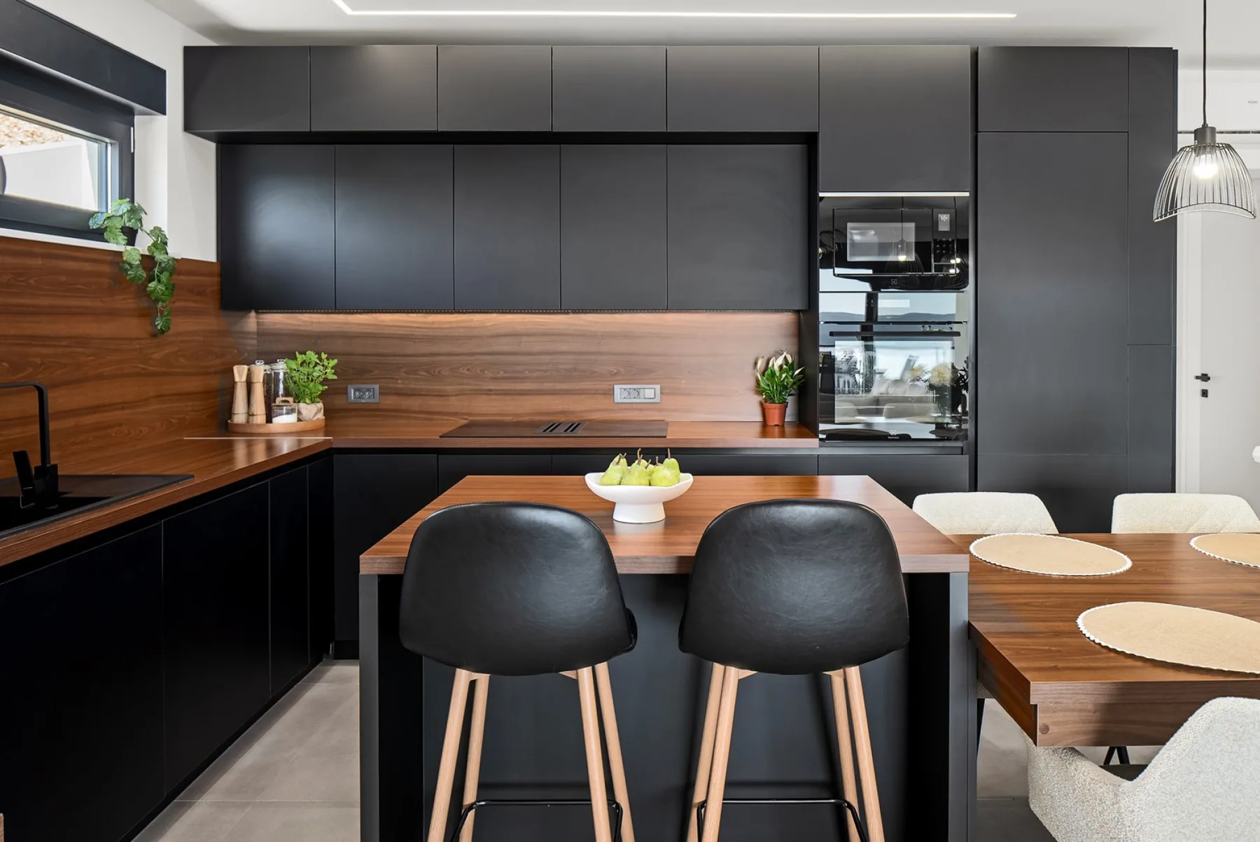 A modern kitchen with dark cabinets, wood-paneled walls, and a central island with bar stools.