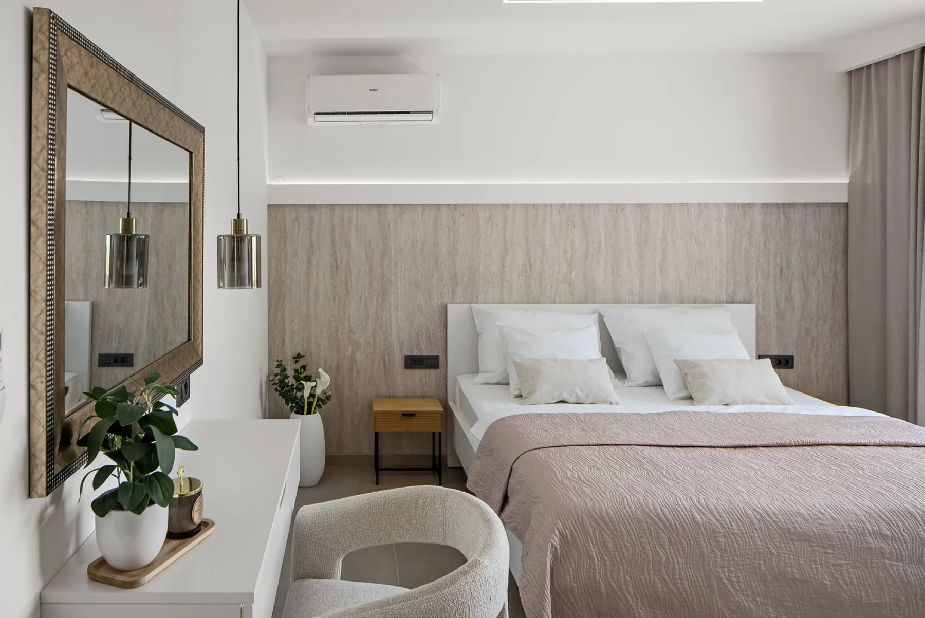 A bedroom with a neatly made bed, upholstered headboard, bedside table, and a potted plant on the dresser.