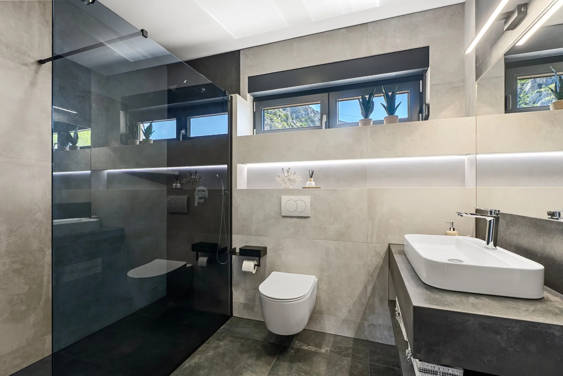 A modern bathroom with a glass shower enclosure, wall-mounted toilet, and white vessel sink.