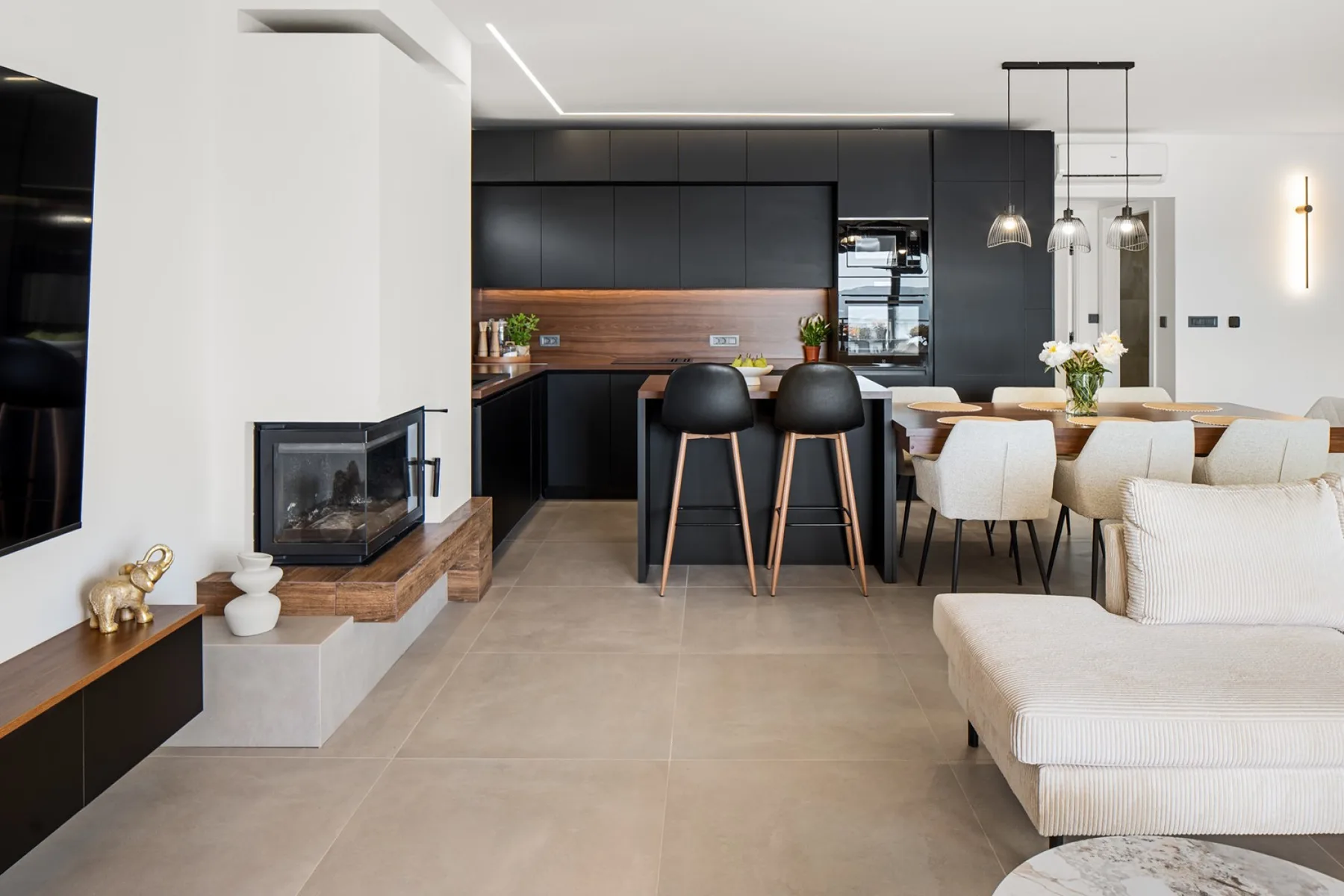 Open-plan living and dining area with a dark kitchen, two bar stools, a dining table, and a white sofa.