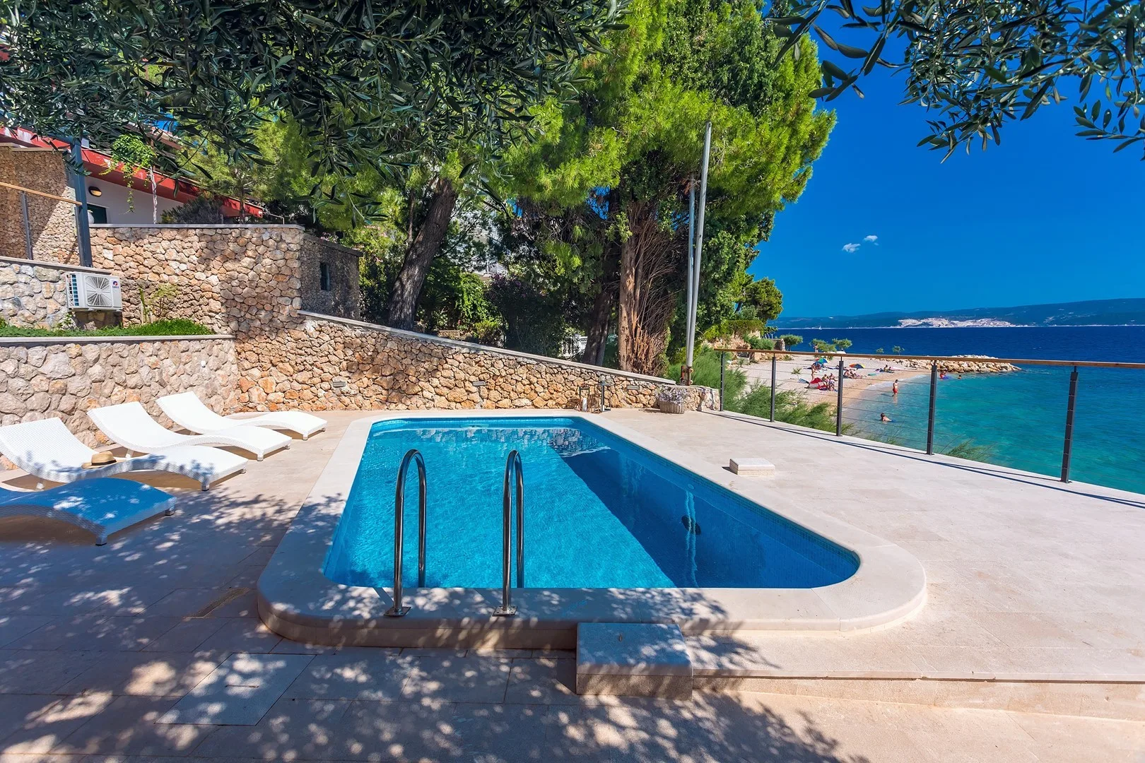A swimming pool and sun loungers overlook the sea beside a stone terrace.