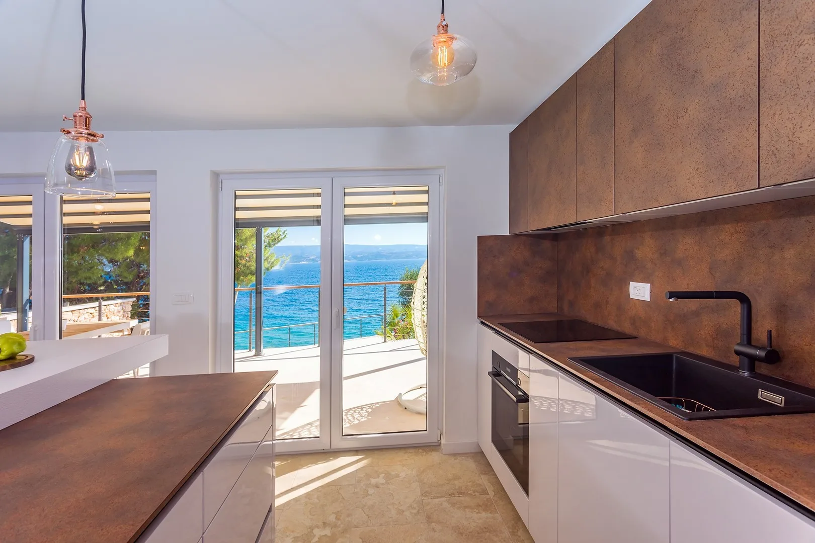 A modern kitchen with dark countertops and sliding glass doors overlooking the sea.