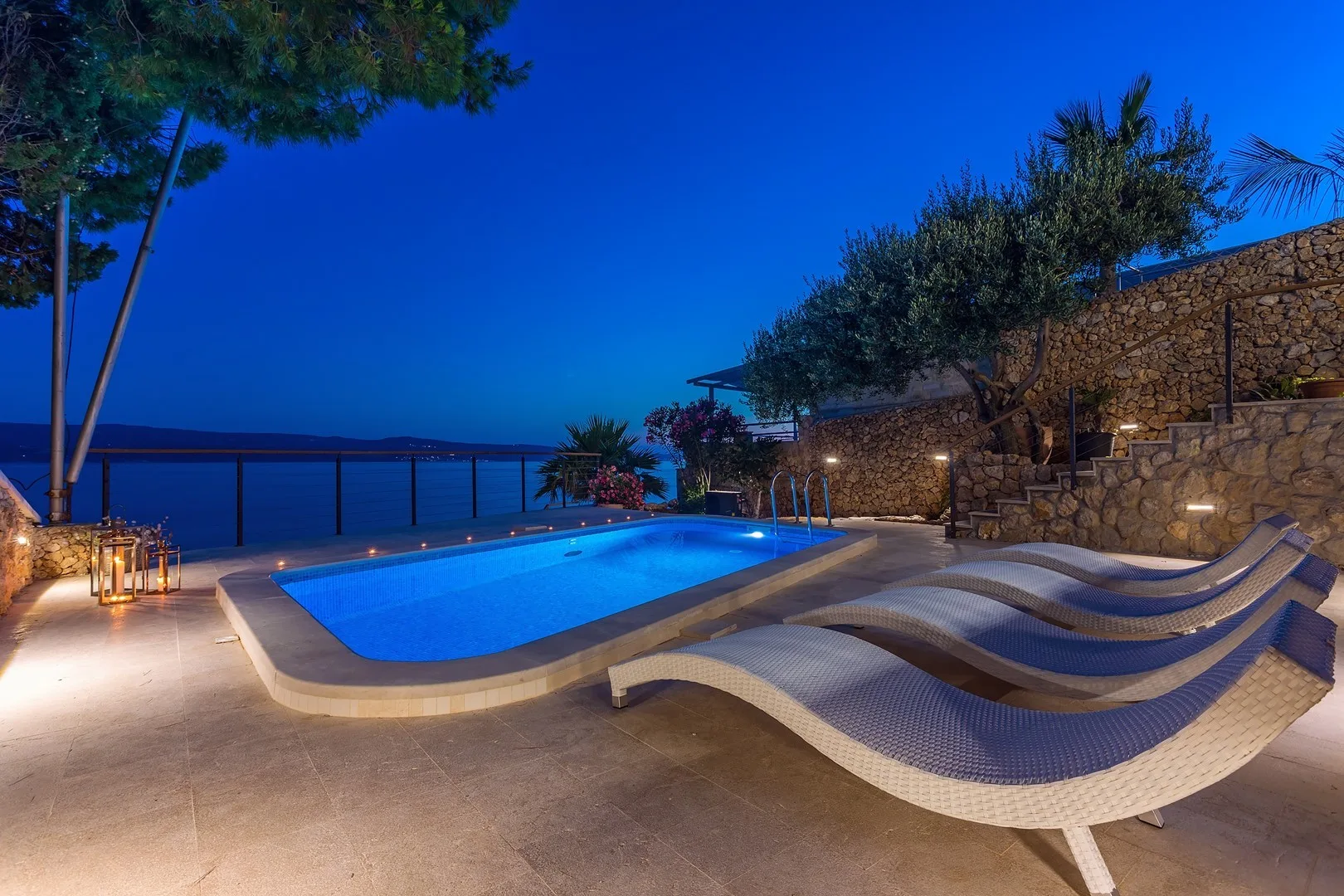An outdoor swimming pool beside the sea, with curved loungers on the patio.