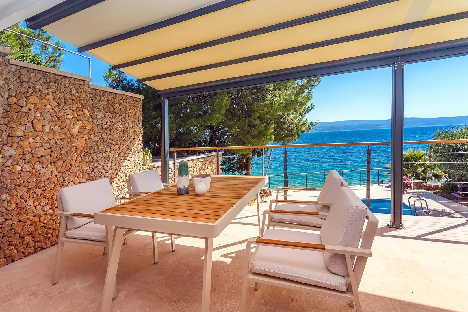 A shaded outdoor dining area with seating overlooks the blue sea.