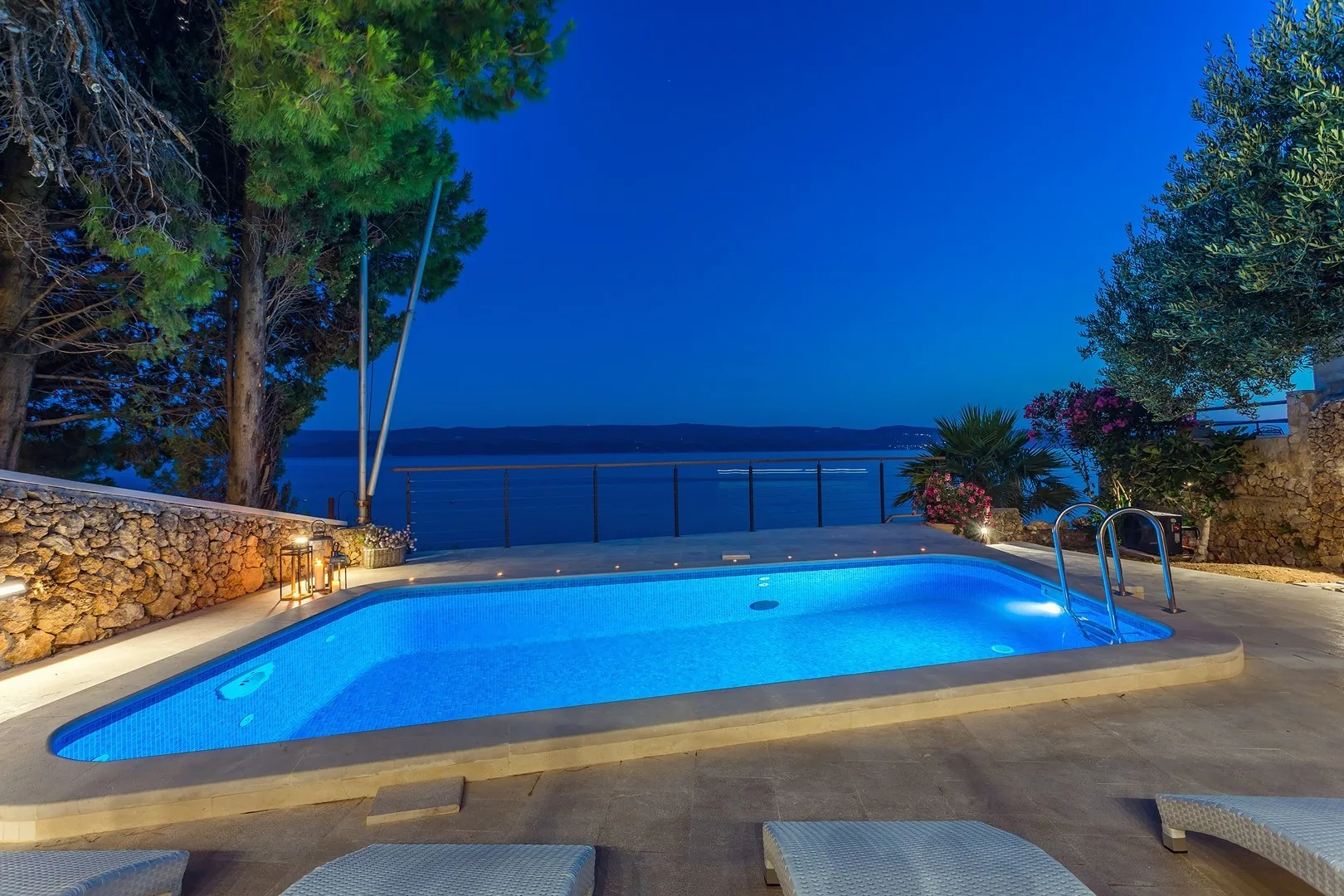 An outdoor swimming pool overlooks the water, with trees and lounge chairs nearby.