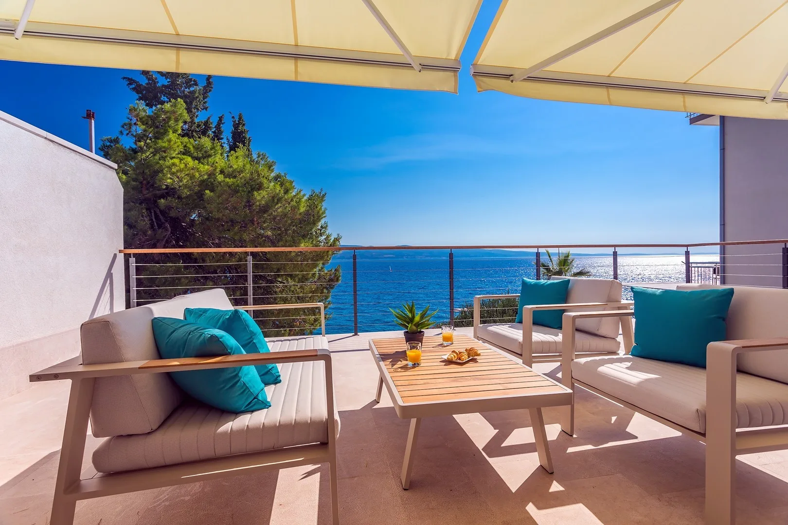 A covered outdoor seating area overlooks the sea, with a low table between the seats.