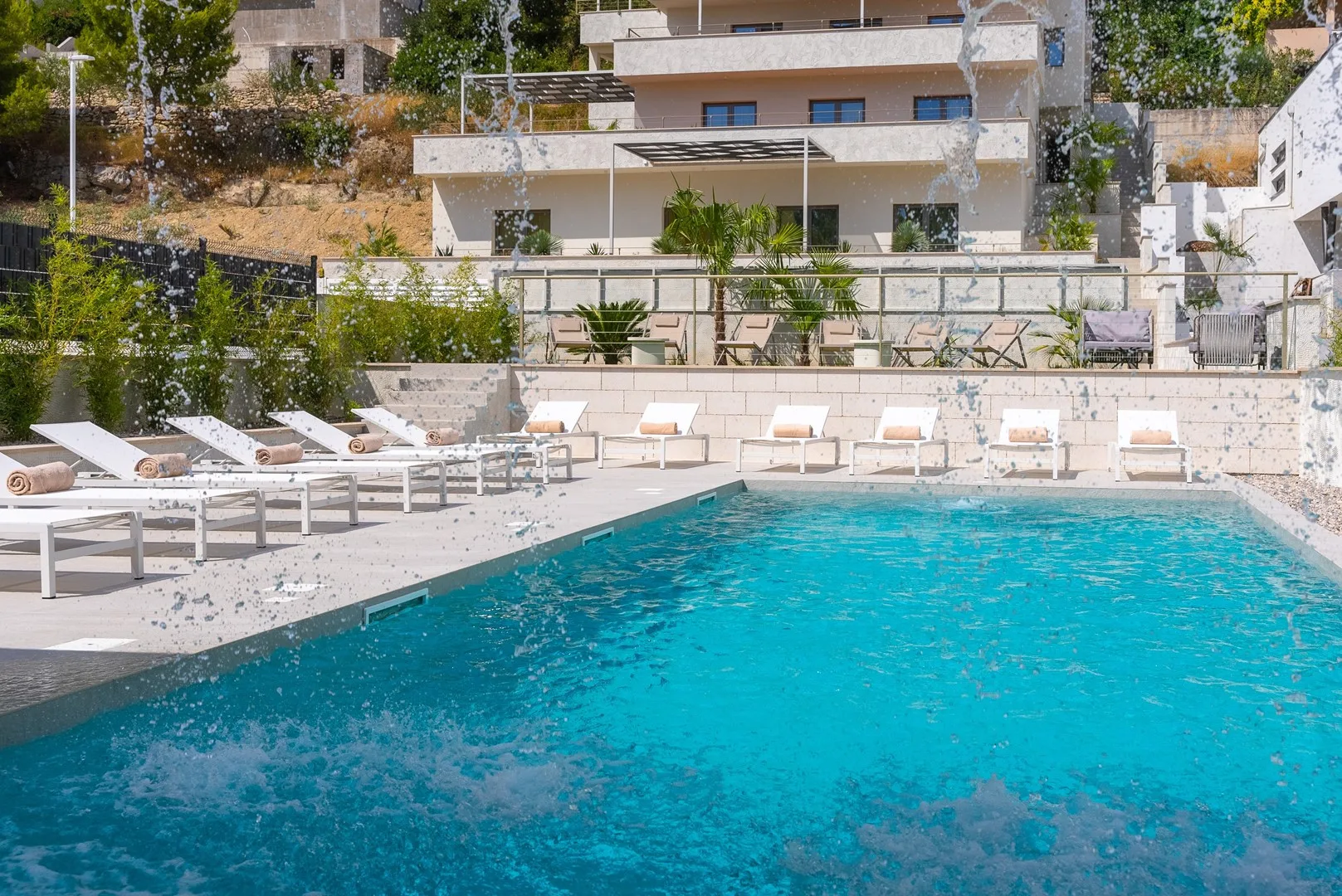 An outdoor swimming pool is surrounded by lounge seating and a modern building.