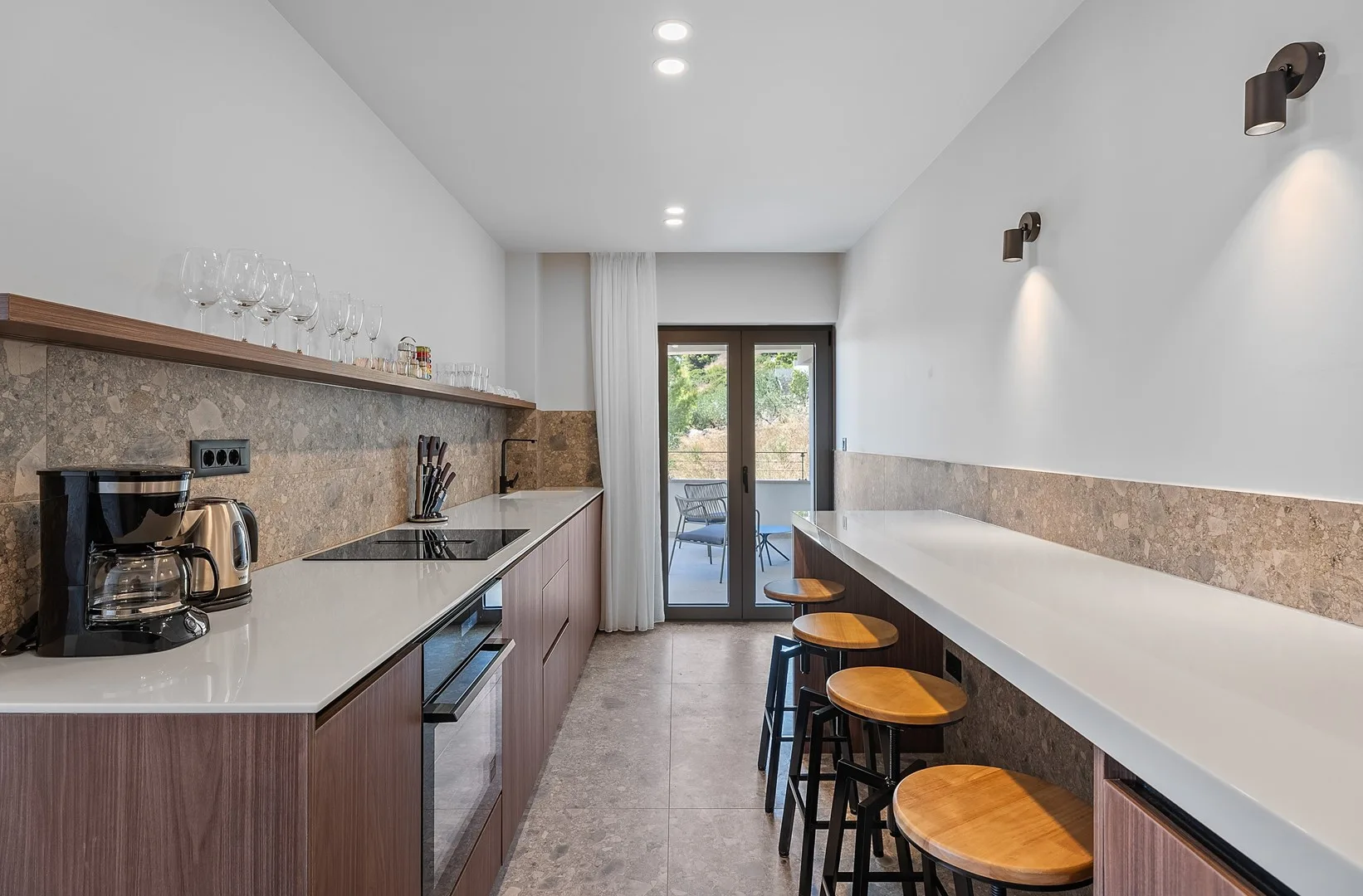 A narrow kitchen with a long counter and glass doors at the far end.
