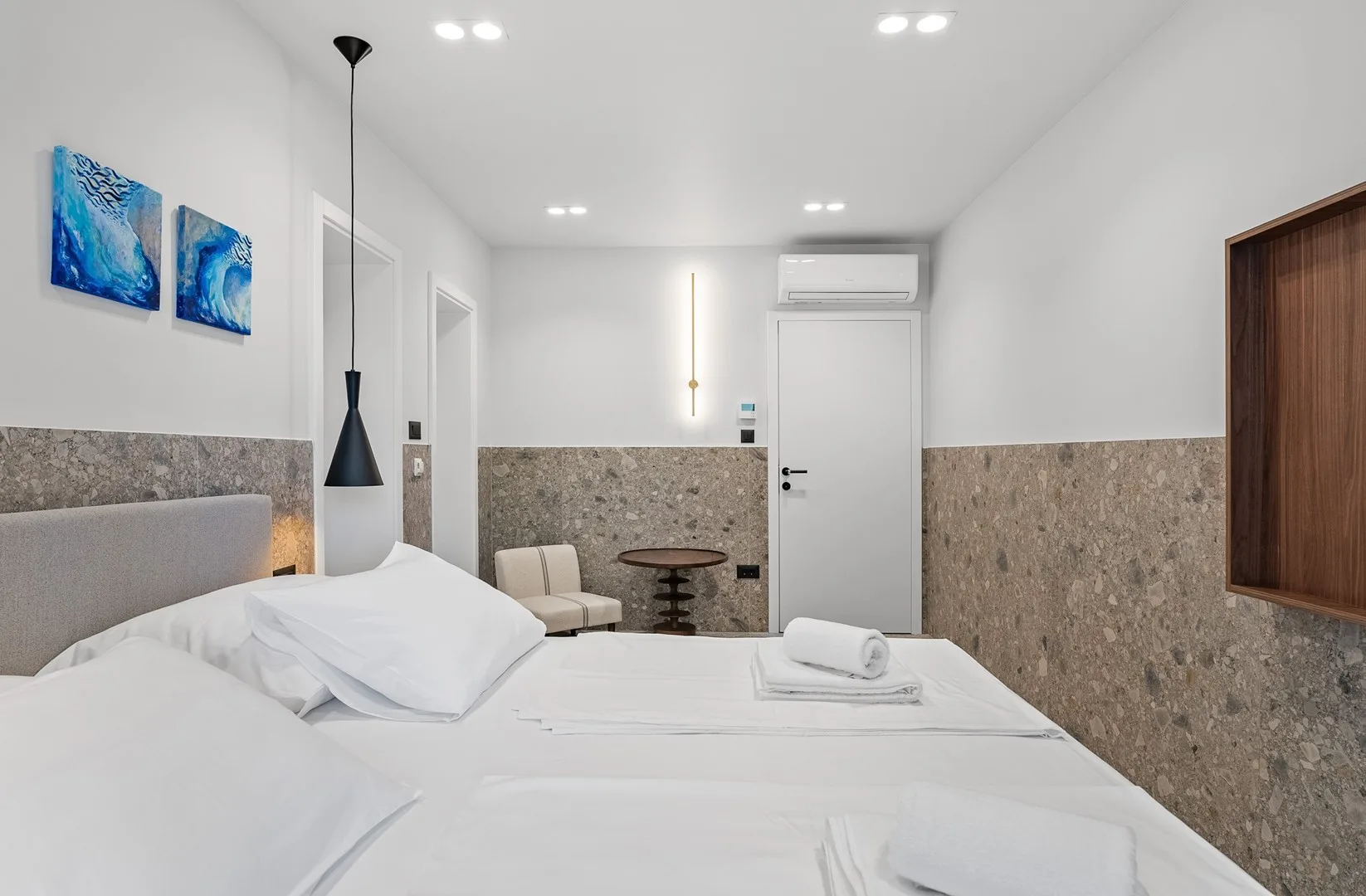 A bright bedroom with white bedding and a small seating area.