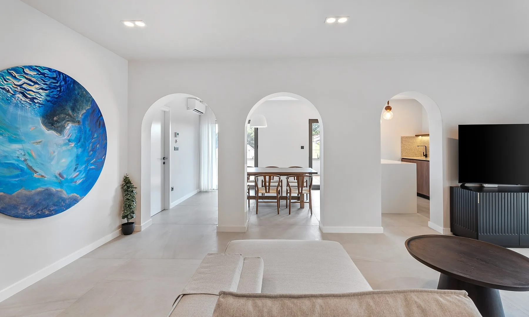 A bright living area with arched openings, a dining table, and a television.
