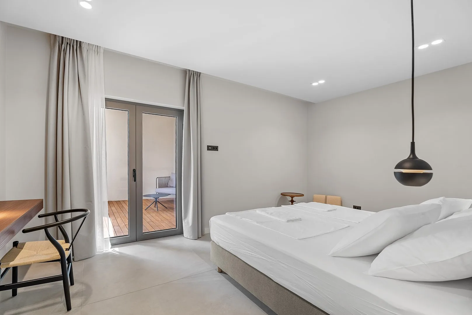 A bright bedroom with a large bed beside glass doors and floor-length curtains.