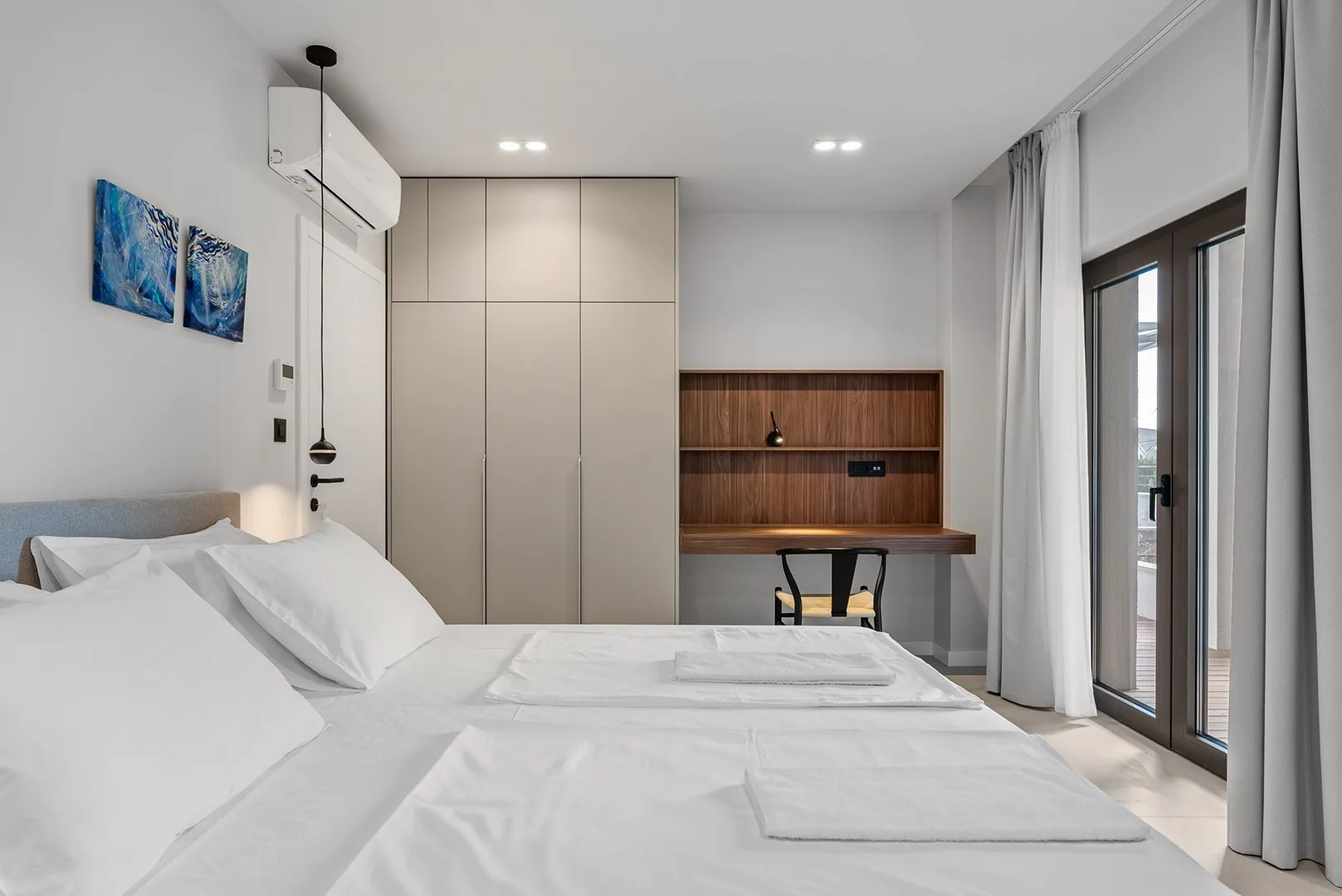 A bright bedroom with white bedding and a built-in desk.