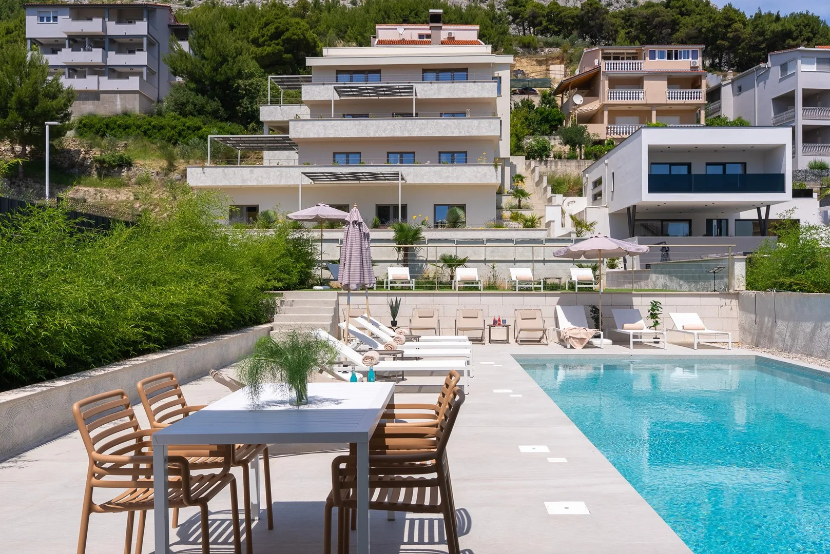 An outdoor pool beside a dining table, with modern buildings in the background.