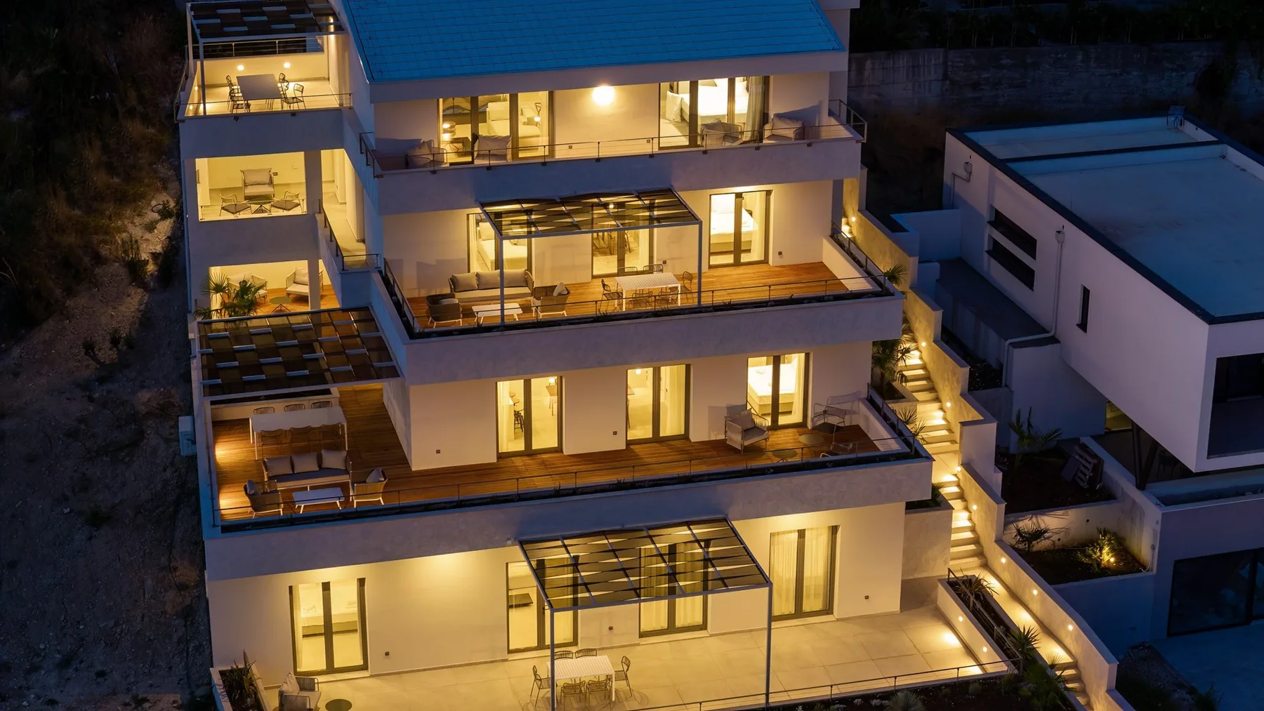 A modern multi-level house glows with warm lights at dusk.