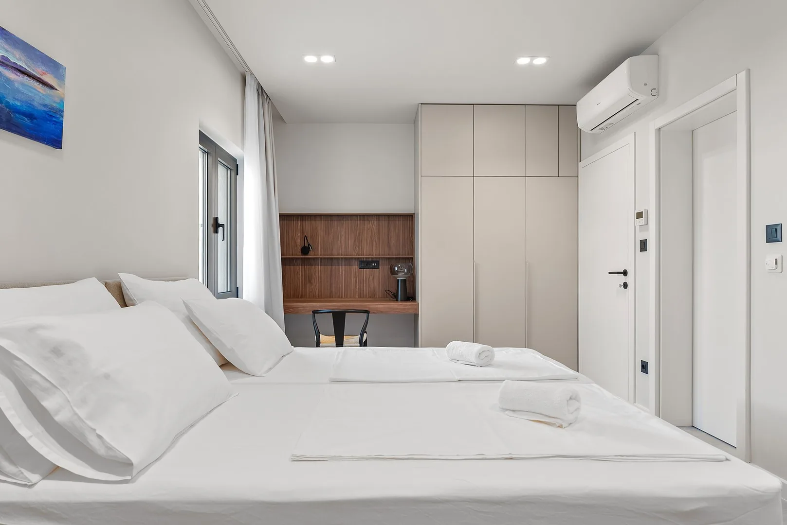 A bright bedroom with white bedding and built-in cabinets.