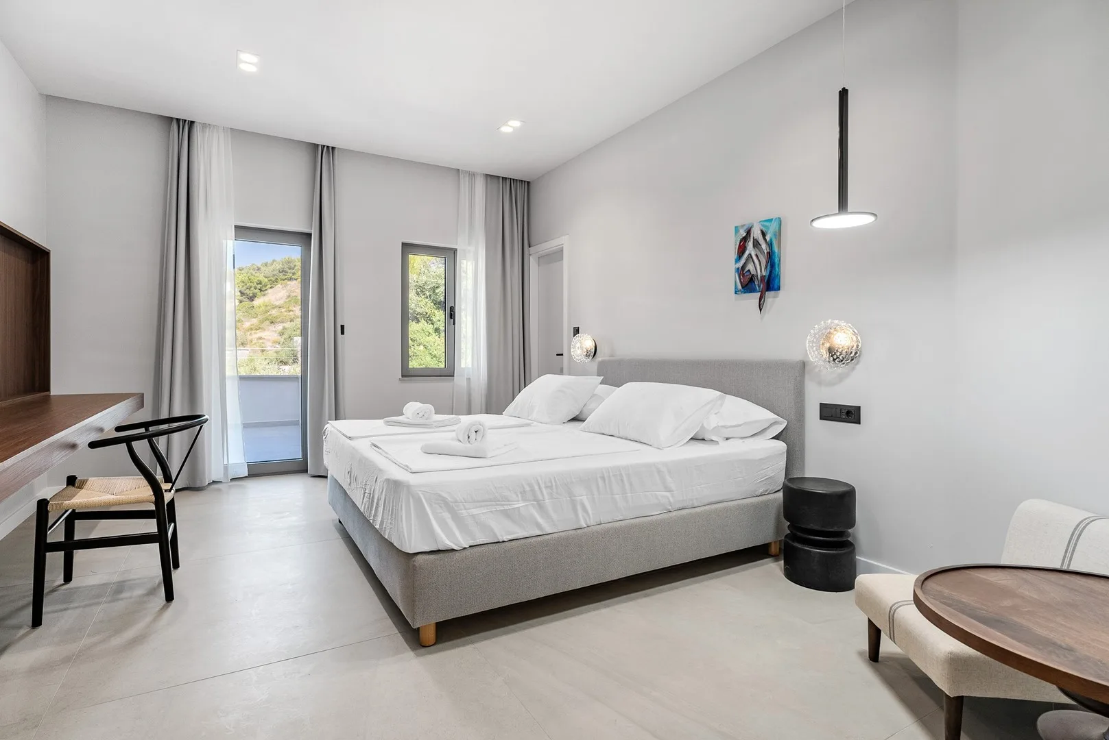 A bright bedroom with a large bed, gray curtains, and a window overlooking greenery.