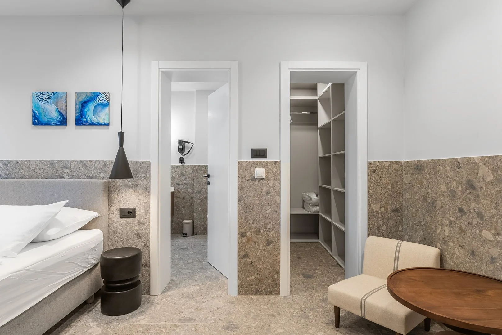 A bedroom with a bed, pendant light, and open doorway to a bathroom.