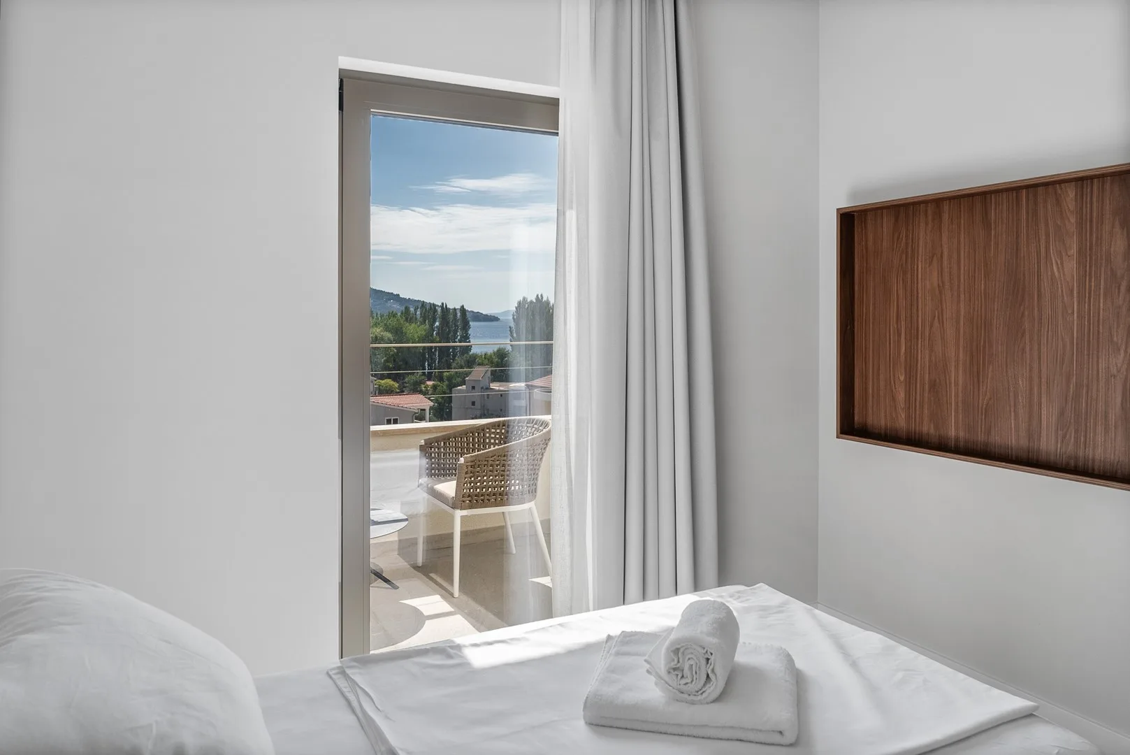 A bedroom with a neatly made bed beside a bright window overlooking the landscape.
