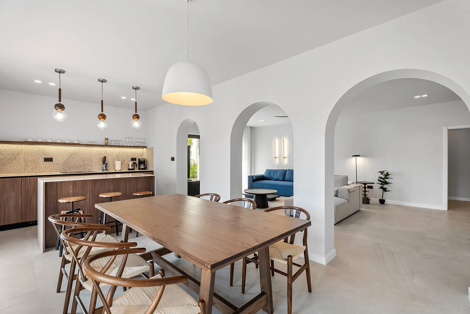 A bright dining area with a long wooden table beside an open kitchen.