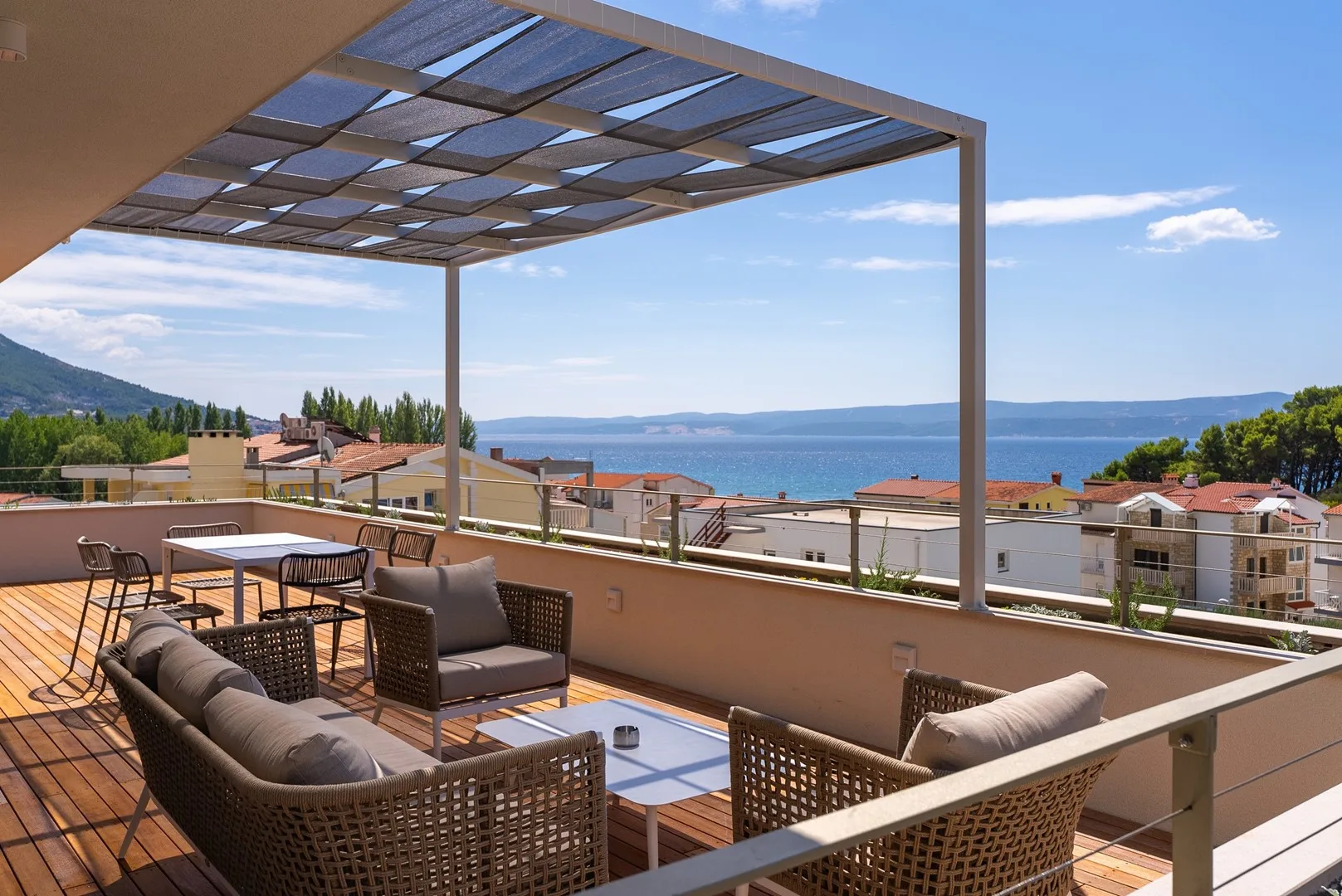 A rooftop terrace has outdoor seating beneath a pergola, with the sea in the distance.