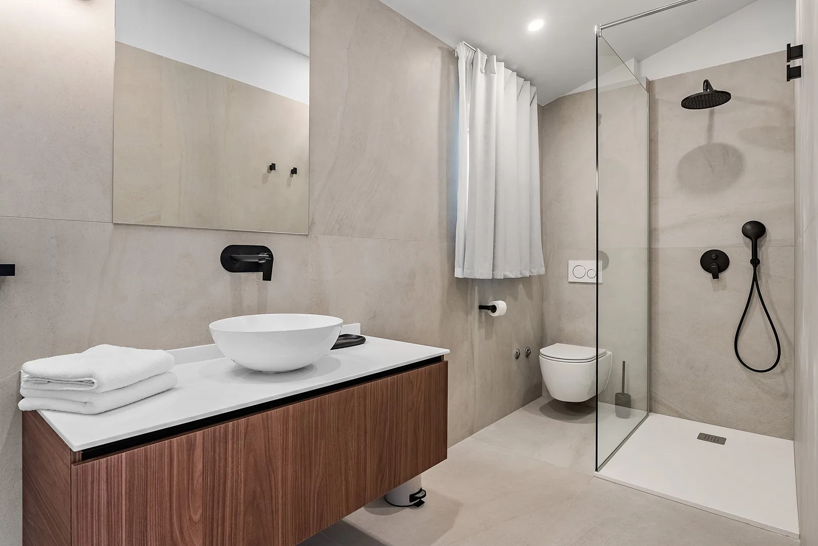 A modern bathroom with a wood-front vanity, vessel sink, and glass shower.