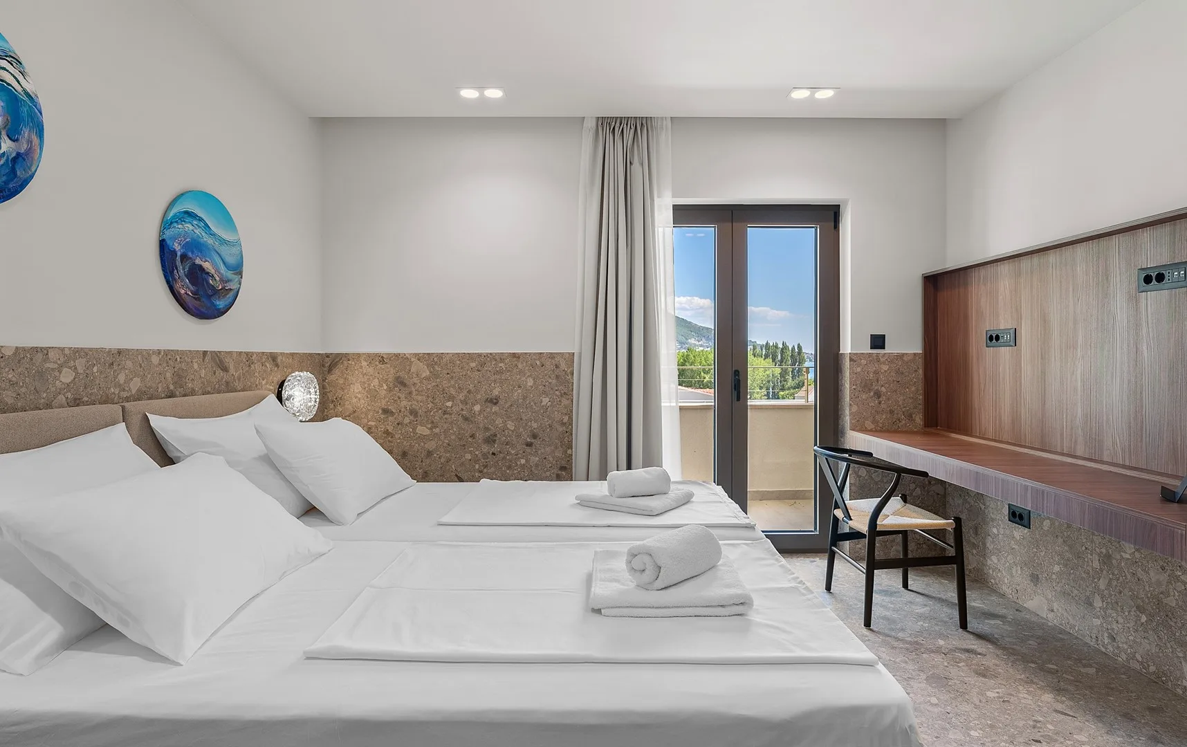 A bright bedroom with neatly made beds and a desk beside the window.