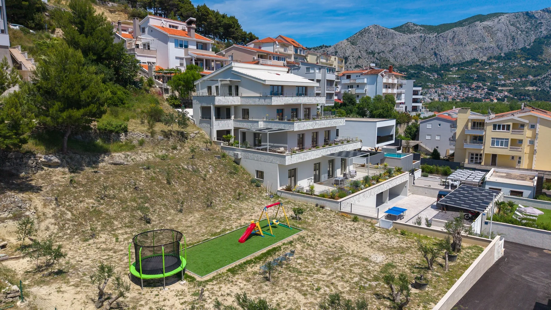 A hillside residential complex overlooks a small playground and the surrounding mountains.
