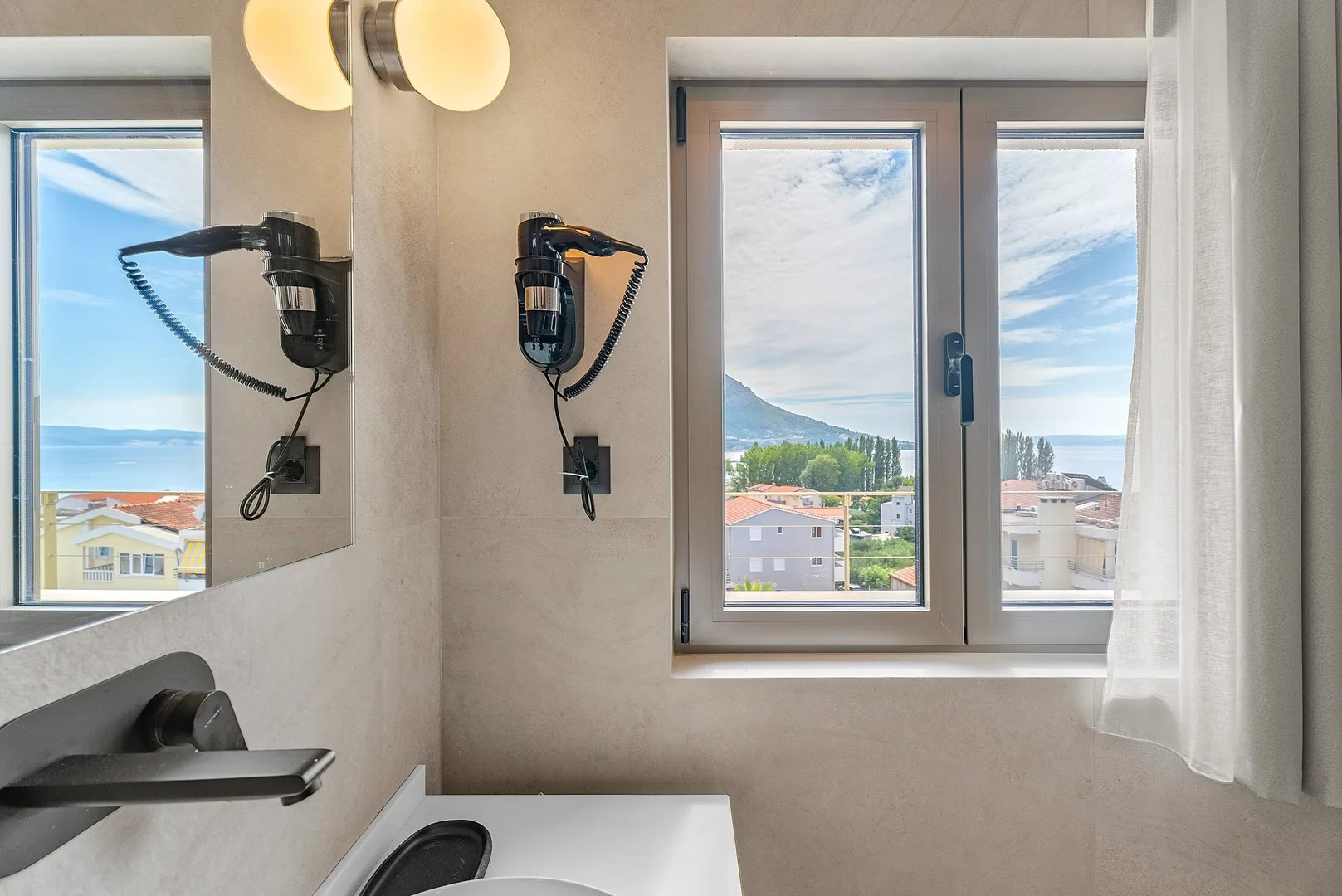 A bathroom with a wall-mounted hair dryer and a window overlooking the water.