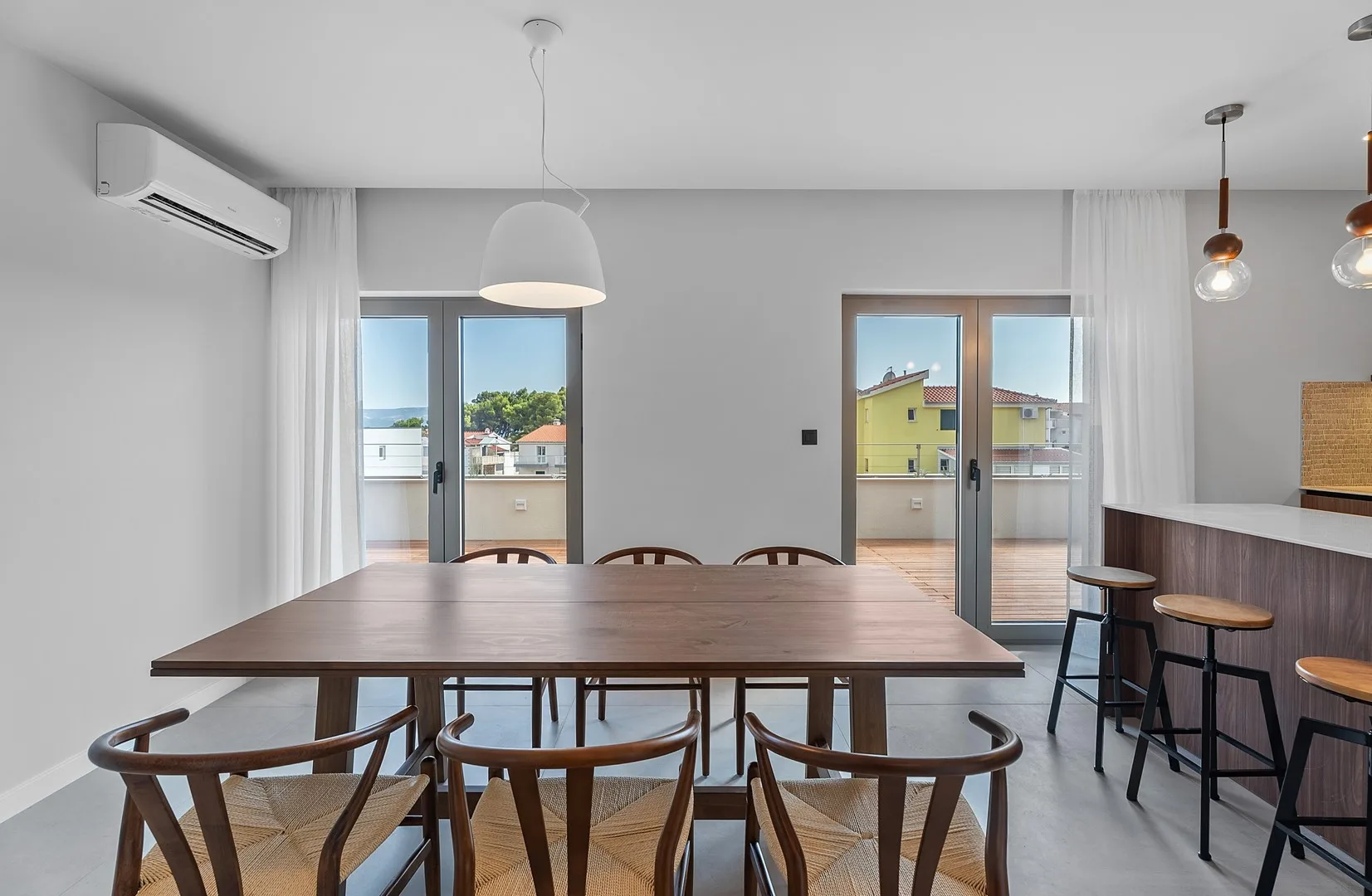 A dining area with a long wooden table and chairs beside glass doors.