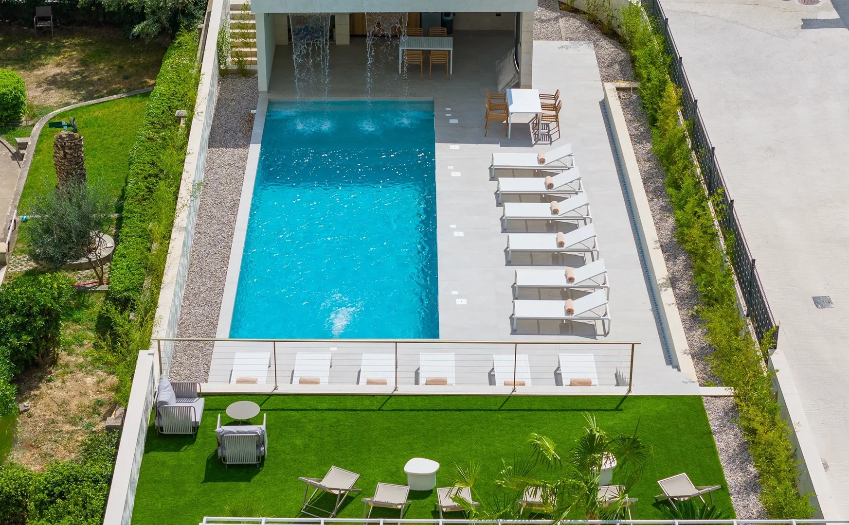 An outdoor pool beside a paved deck with lounge seating and green lawn.