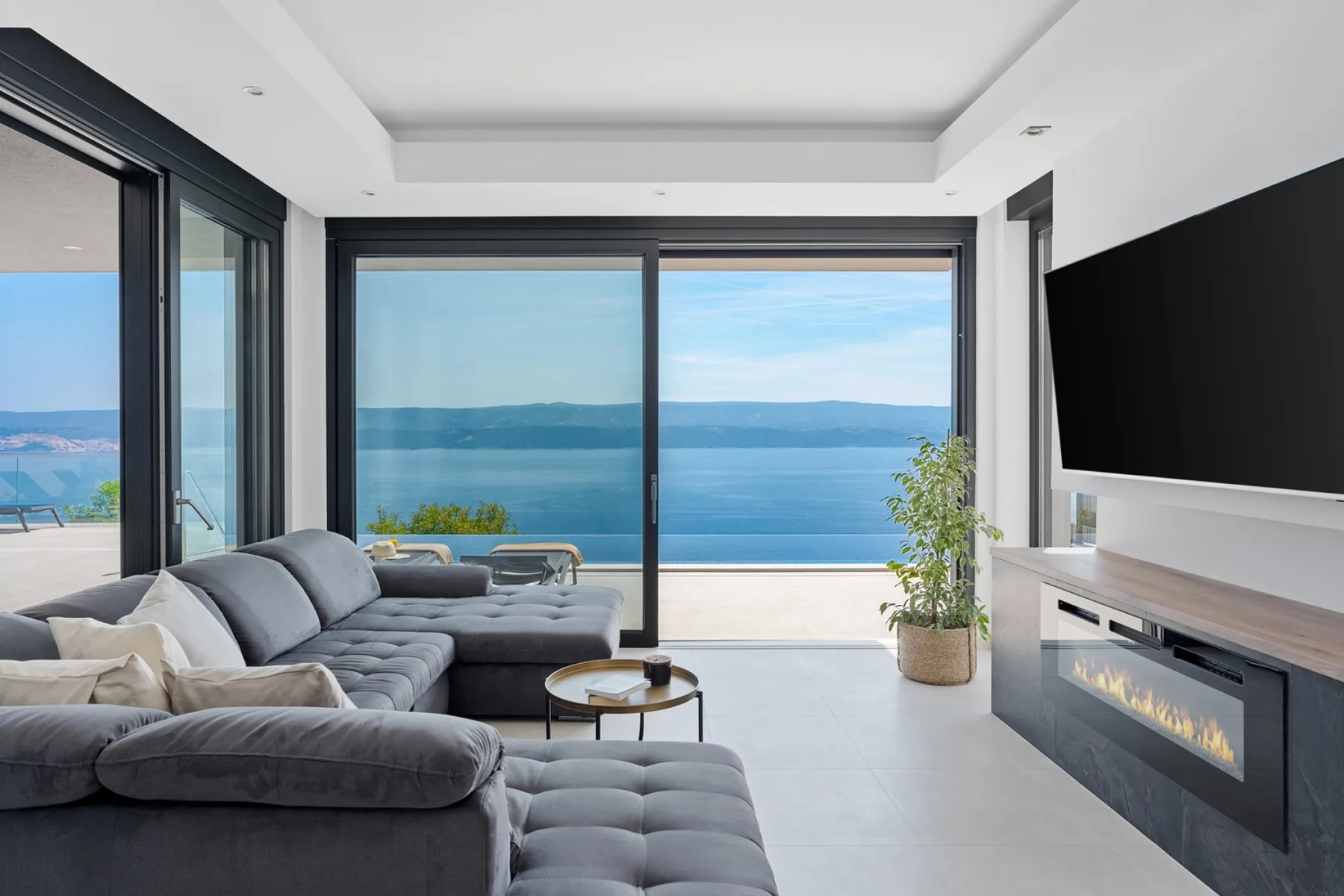 A modern living room opens onto a large window overlooking the water.