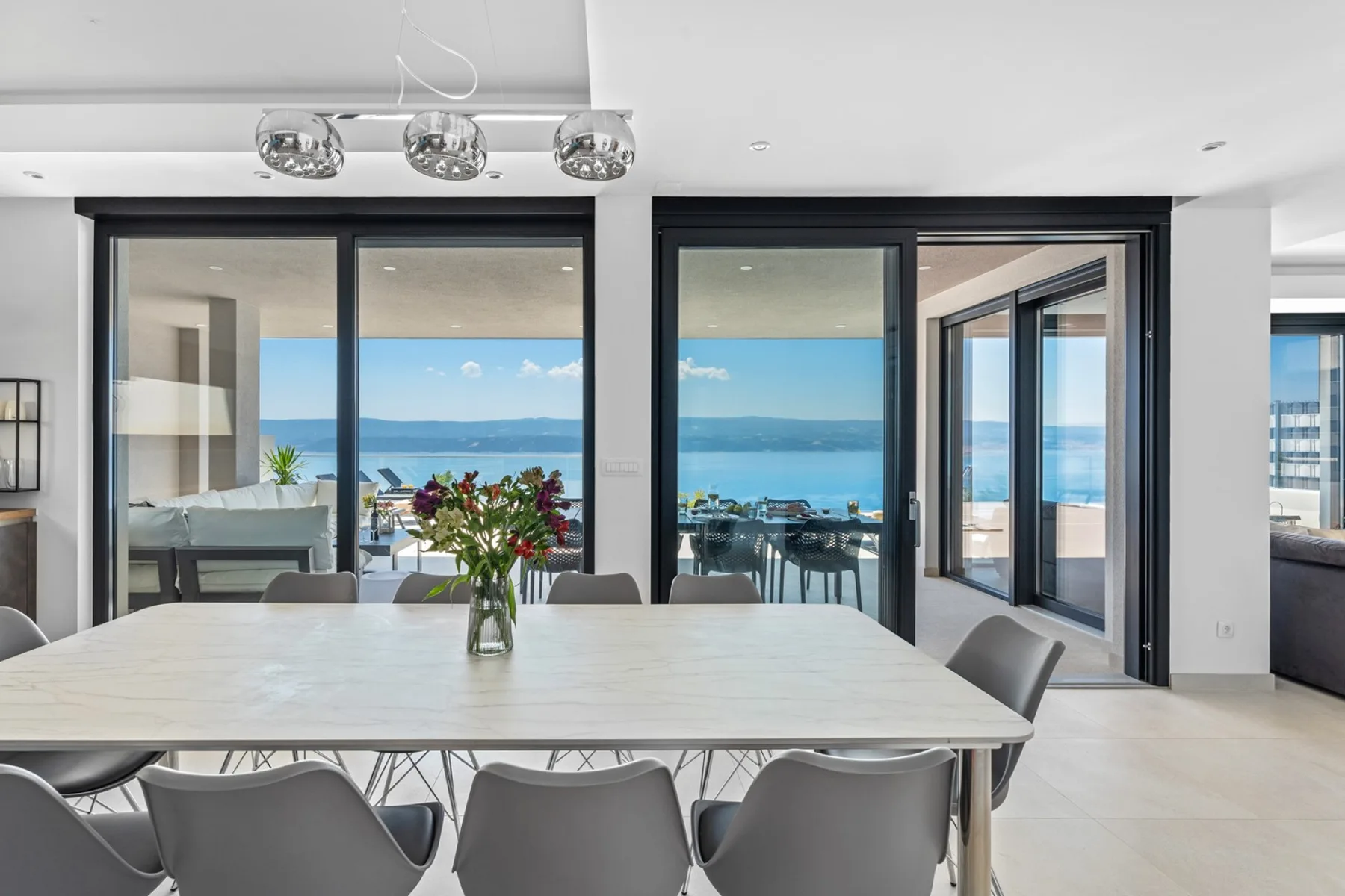 A bright dining area with a large table and ocean views through glass doors.