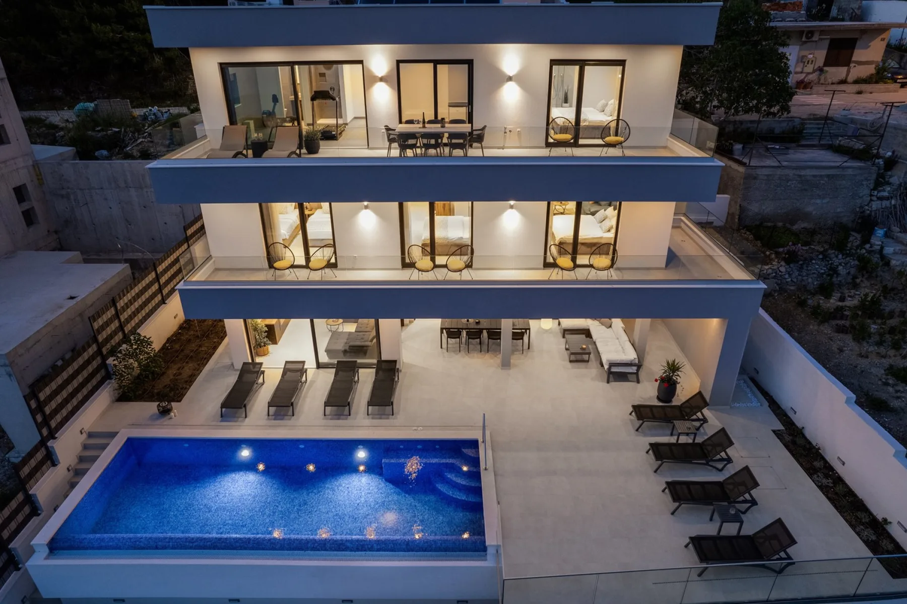 A modern multi-level building with balconies overlooks a swimming pool and outdoor seating.