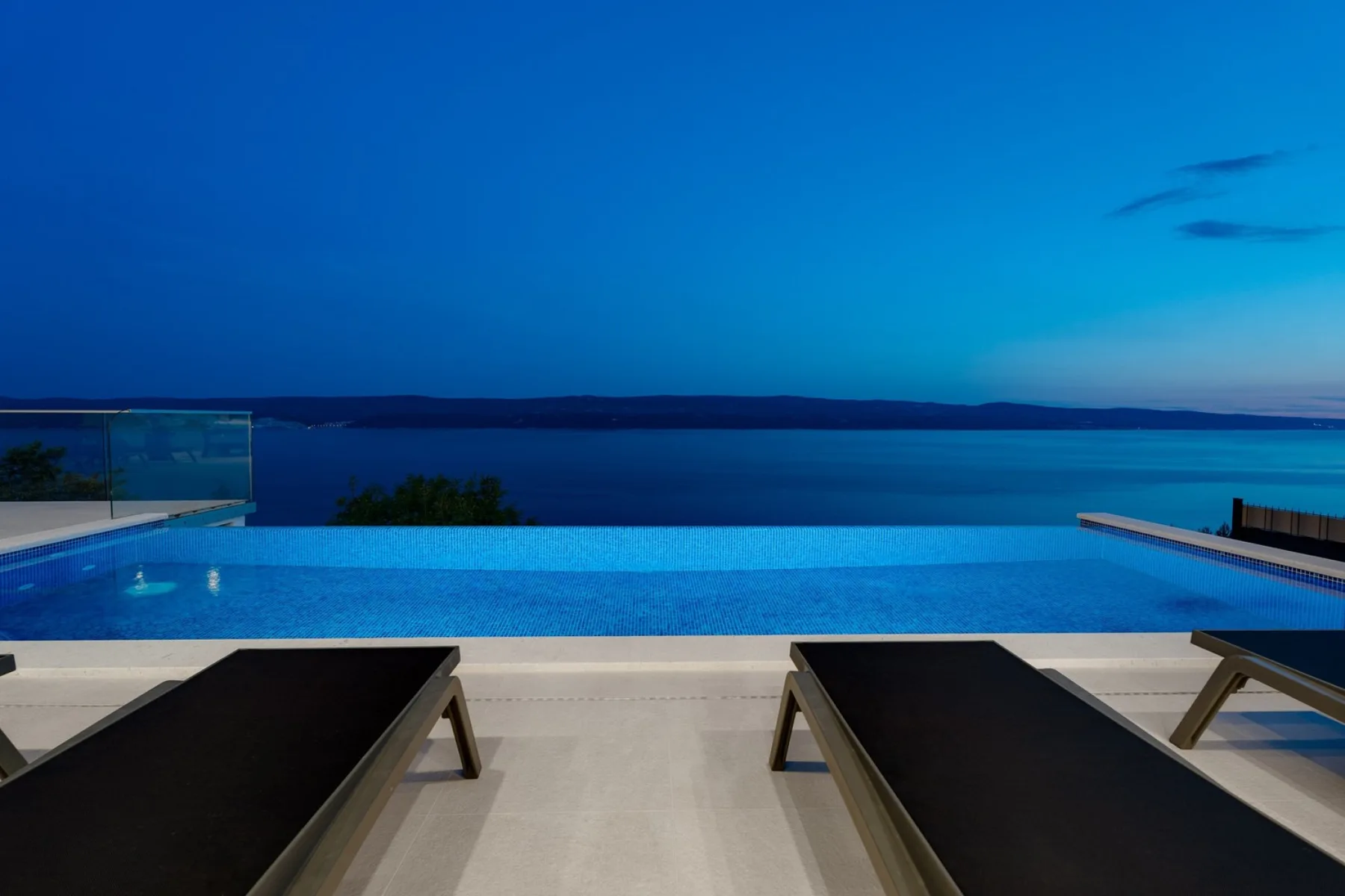 An infinity pool overlooks the water at dusk, with lounge seating along the deck.