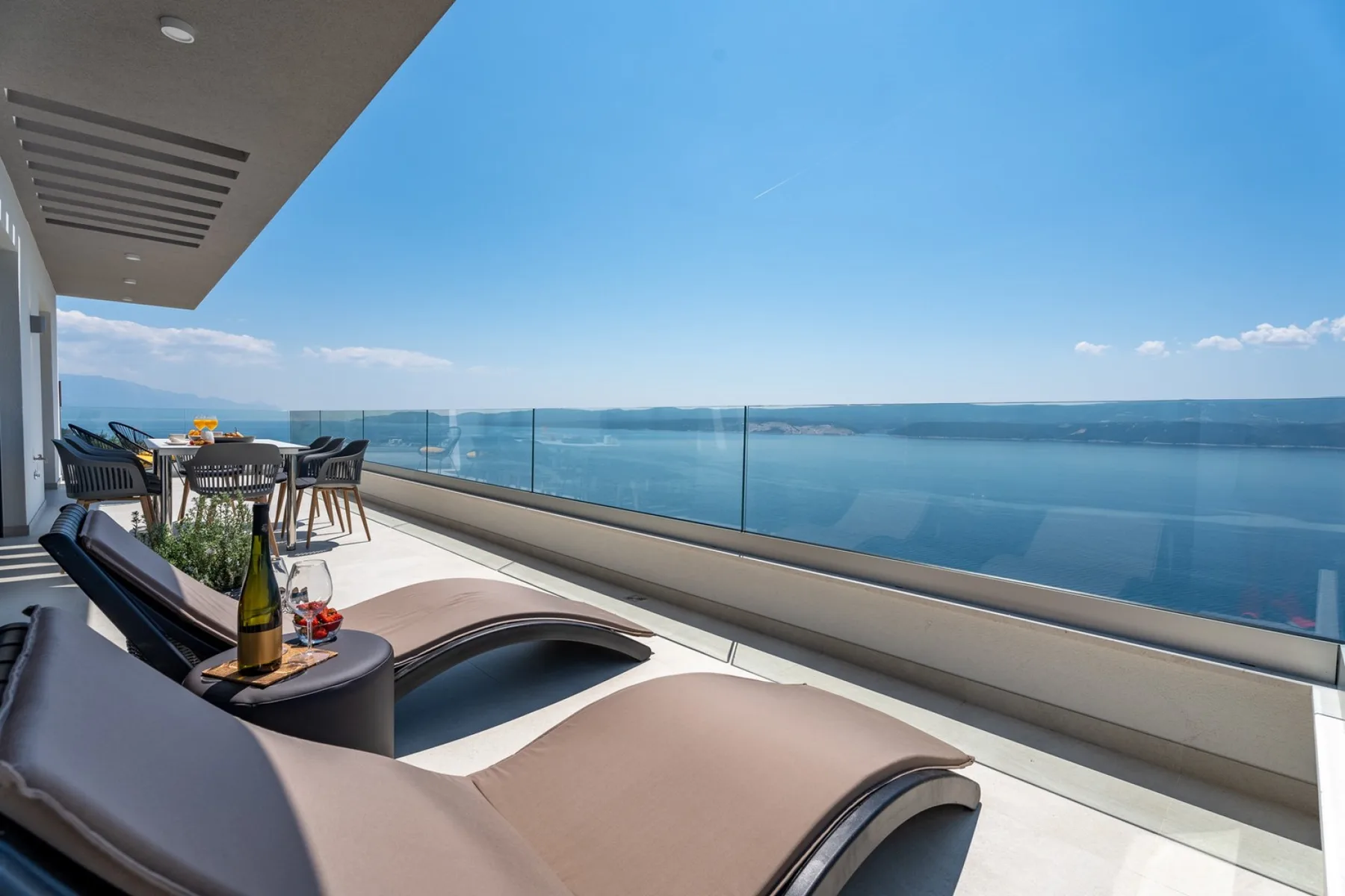A waterfront terrace with lounge seating and a glass railing overlooks the water.