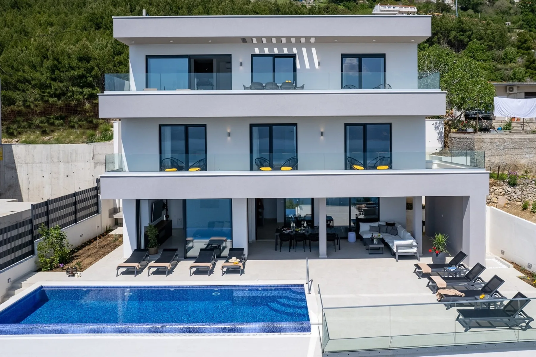 A modern multi-level house overlooks a swimming pool and outdoor seating area.