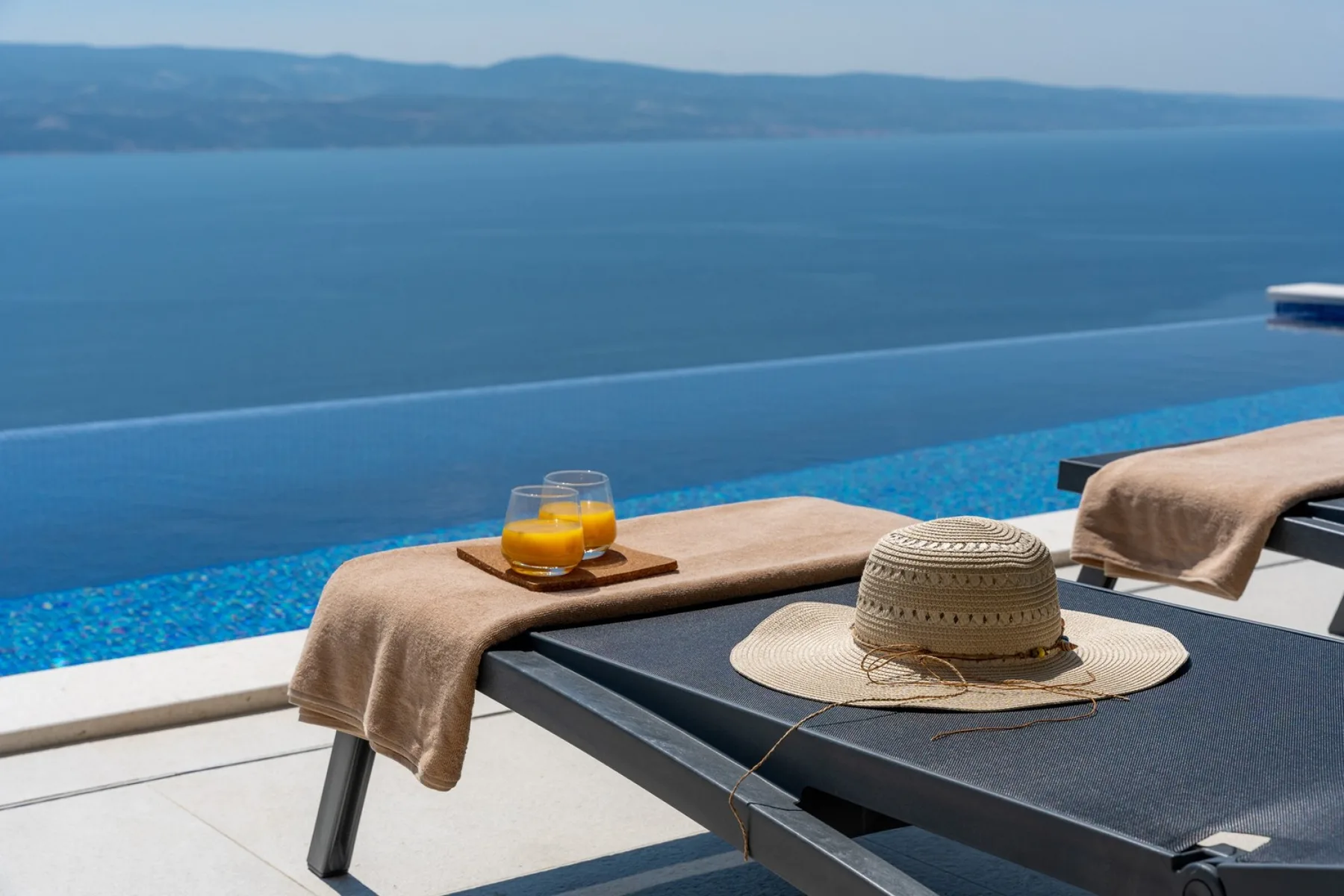 Poolside seating overlooks a blue infinity pool and distant shoreline.