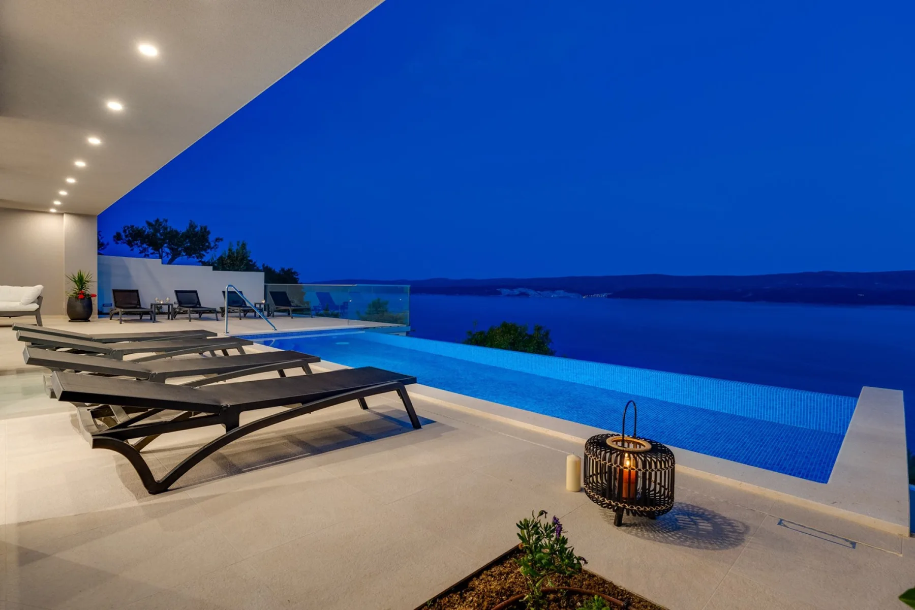 A poolside terrace at dusk overlooks the water, with lounge seating beside the pool.