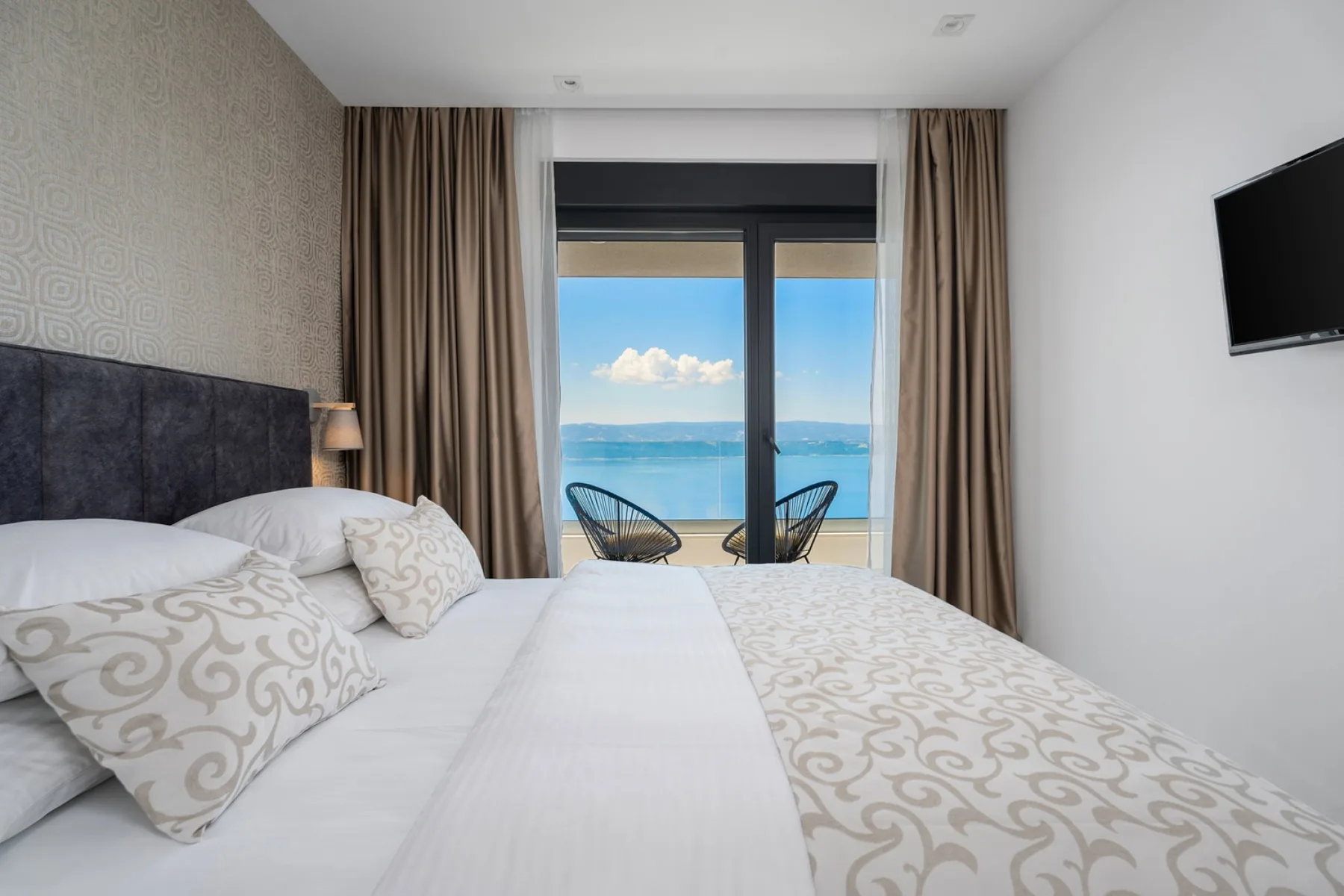 A bedroom with a large bed facing glass doors and a view of the sea.