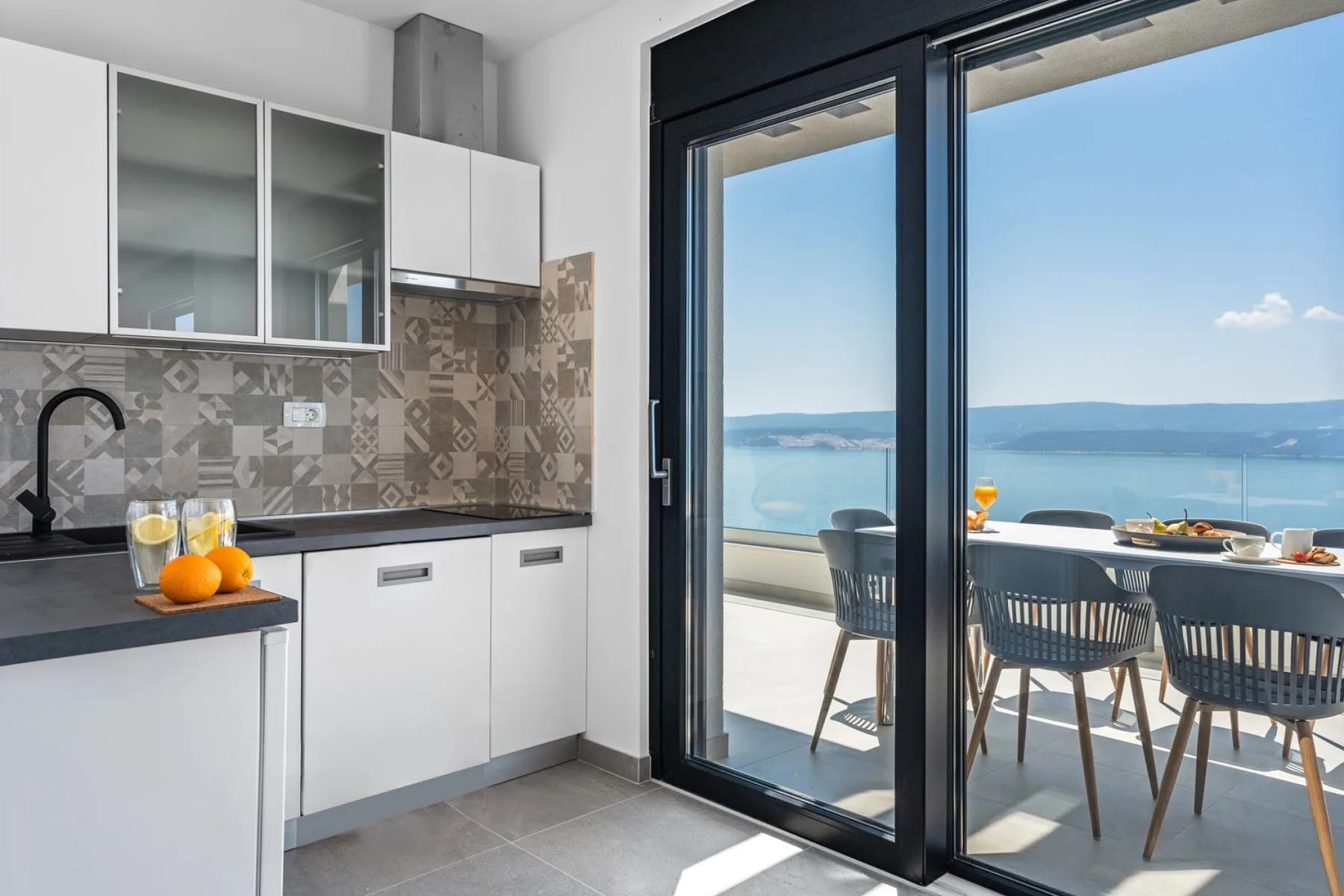A modern kitchen opens onto a dining area with a view of the water.